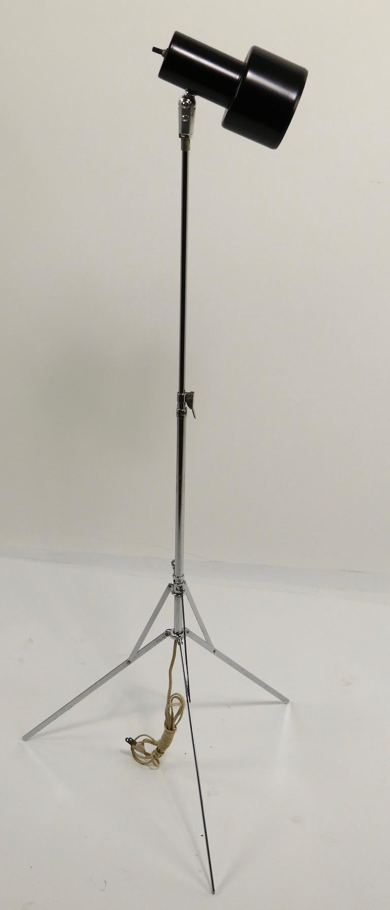 Vintage adjustable chrome base lamp by Luxo. This lamp has an articulated folding easel base which can be extended in height (58-32 inch) and a black hood shade (7.5 inch) that tilts and pivots to direct the light. The lamp is in clean, working