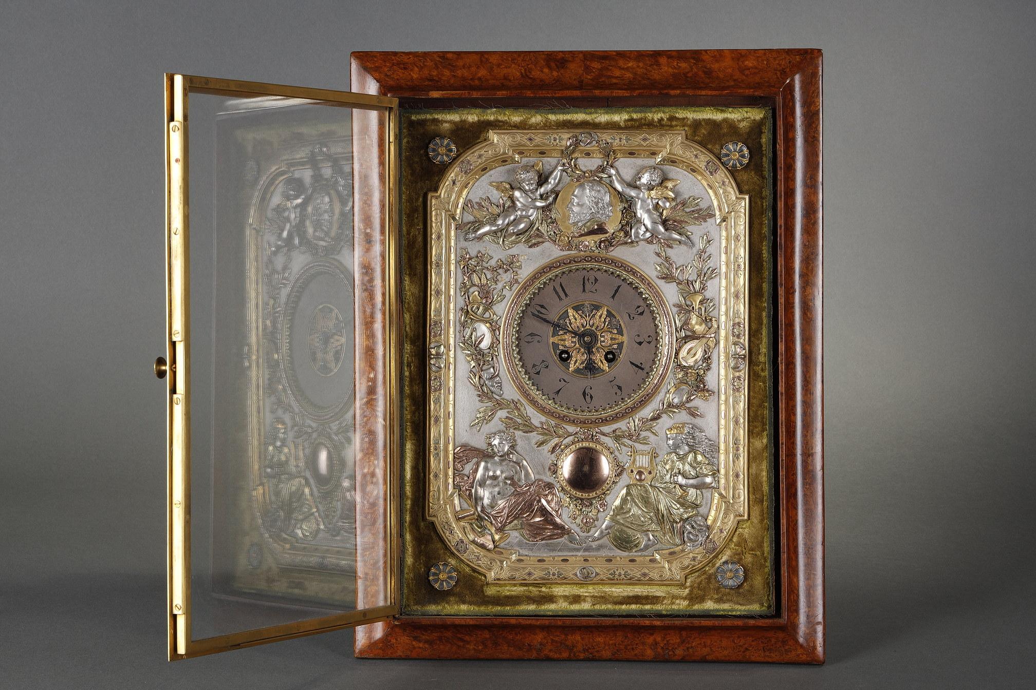 Signed Elkington & Co
Numbered Rd 92173

Beautiful rectangular table clock executed in gilded and silvered electrotyped metal, decorated in relief with butterflies, music instruments and theater masks, surmounted by two angels crowning with a