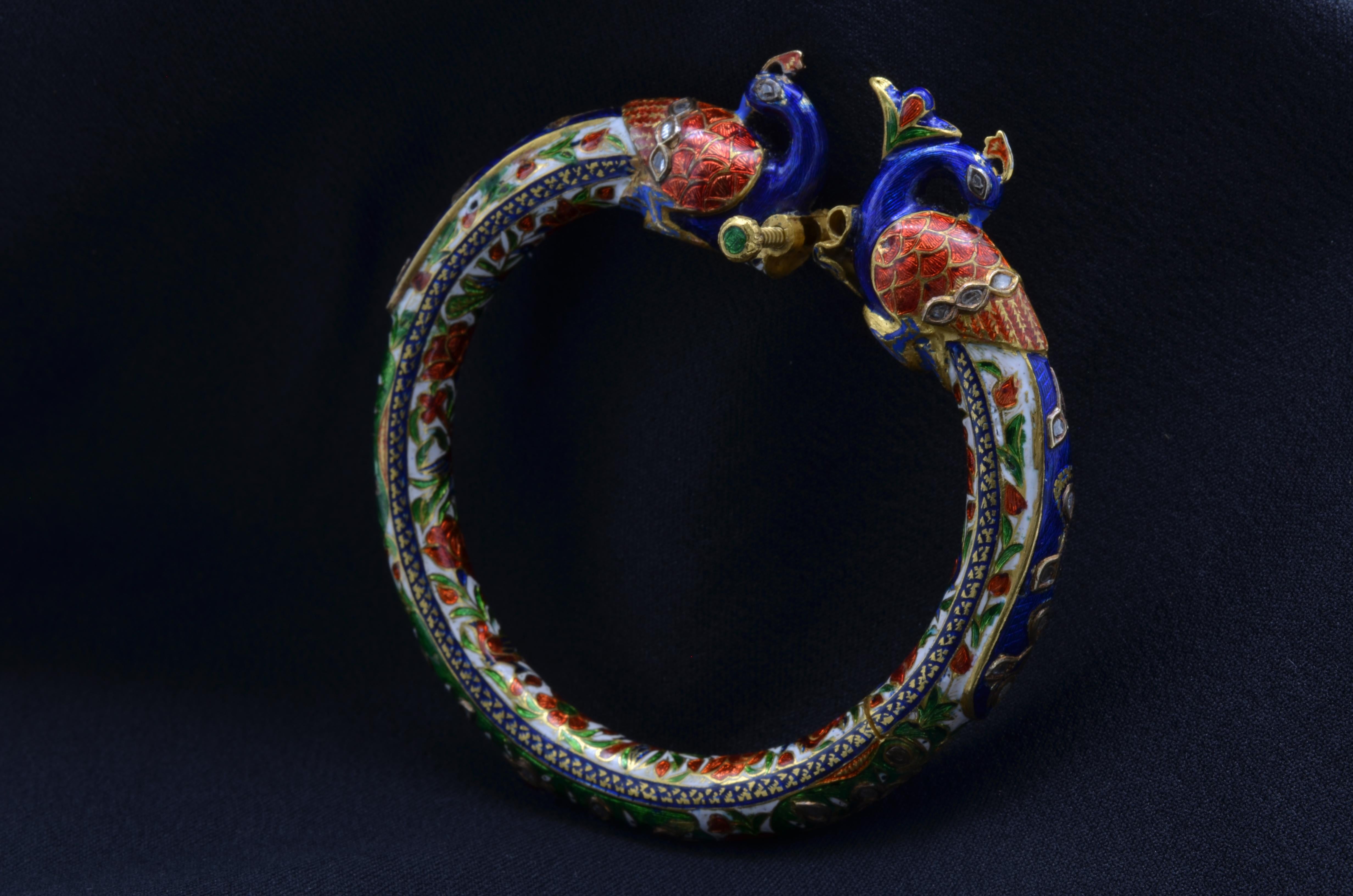 This fantastic antique peacock bangle from the Mughal period was made in the mid-late 1800's and is complete with red, blue, and green enamel on  22K yellow gold. There are gold engravings on all sides of the four hinges. The head of the peacocks