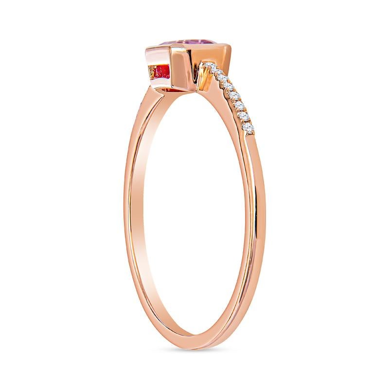 This dainty ring features an emerald cut pink sapphire set east-west accented by 0.05 carat total weight in round diamonds on the band set in 14 karat rose gold. It is a size 6.5 but can be resized upon request. This ring can be worn alone or