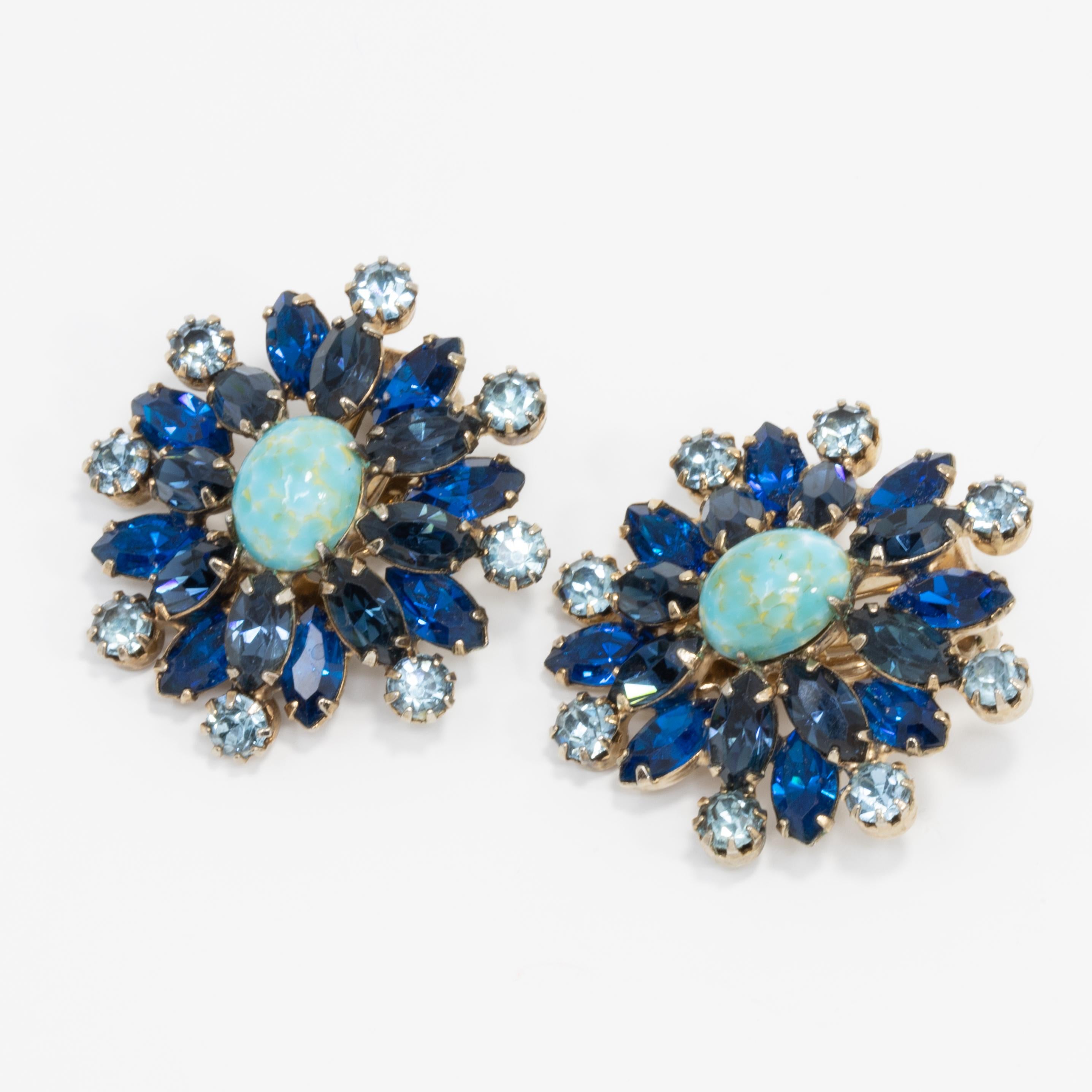 A pair of glowing blue clip on earrings, featuring a Easter turquoise-colored cabochon, decorated with aquamarine and sapphire crystals. All prong-set in a light gold-tone setting.

Circa mid 1900s.