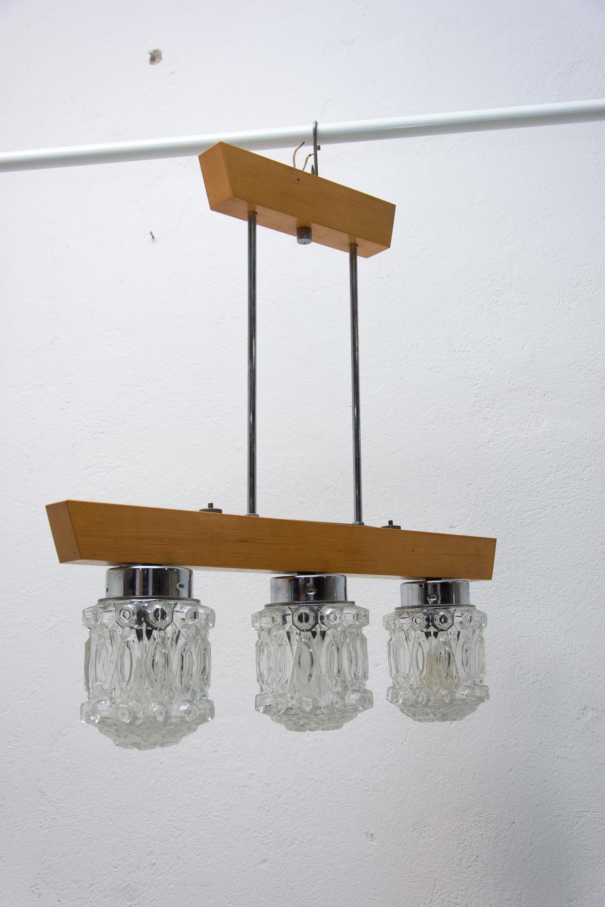 This chandelier comes from a Czechoslovak hotel and comes from the so-called Brutalist era of the former Eastern bloc in the 1970´s. It´s made of cut glass and wood.
It has a wooden structure and six cut glass lampshades. The pendant is in very