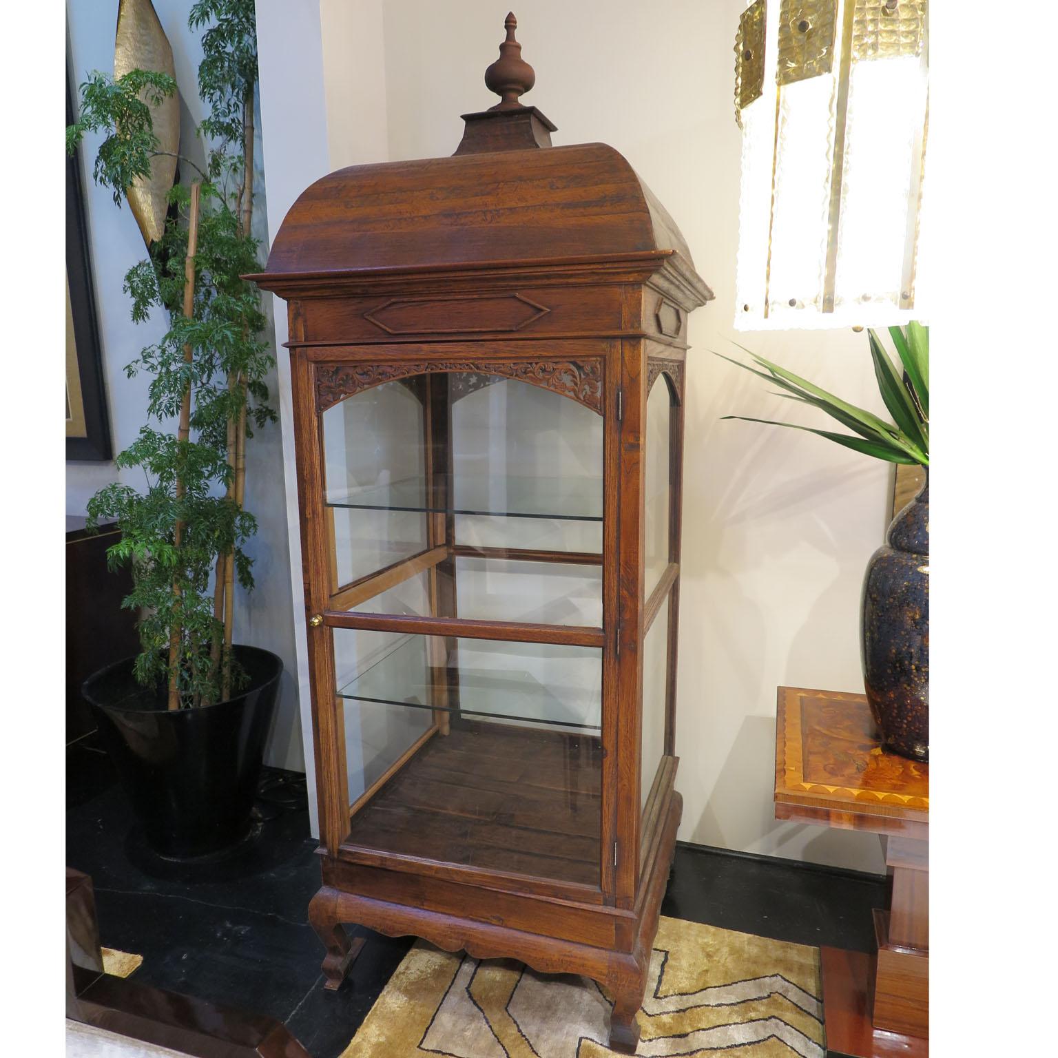 This 20th century wooden vitrine stems from Eastern Europe. The glass panel enclosure features two glass shelves. Above the door sits an ornately carved detail of latticework. The curved roof displays a decorative finial.