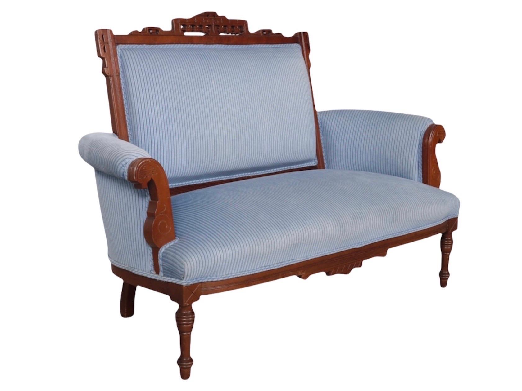 An Eastlake period settee surmounted with a pierced crest rail is carved with a simple floral motif, the shape mirrored in the skirt pediment. Outward rolled arms are finished with wooden panels carved with scrolled details. Round legs taper