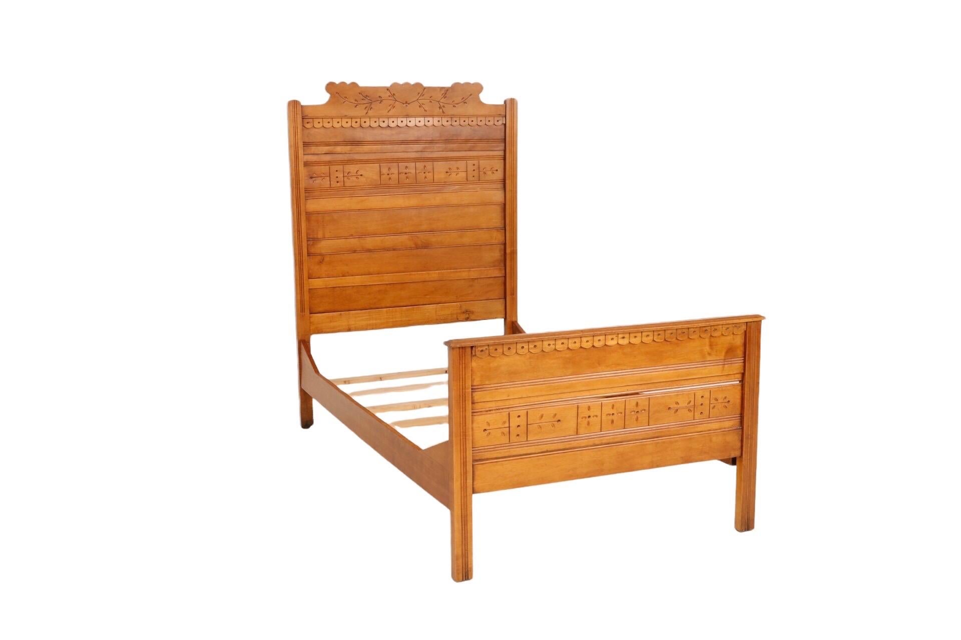 A hand carved Eastlake period twin bed made of solid walnut. The headboard pediment is decorated with elegantly carved branches and spoon shaped leaves. The headboard and footboard are trimmed with a row of applied scalloped buttons. Below, a