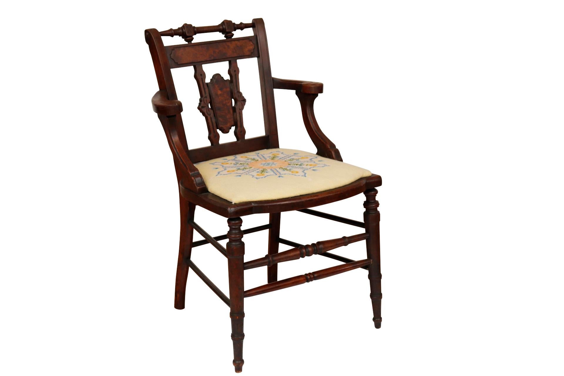 An antique Eastlake side chair. The shield shaped seat is upholstered with a floral needlepoint. Square x carved finials top the crest rail, above a horizontal splat decorated with a burlwood cartouche. The back splat is made with two supports
