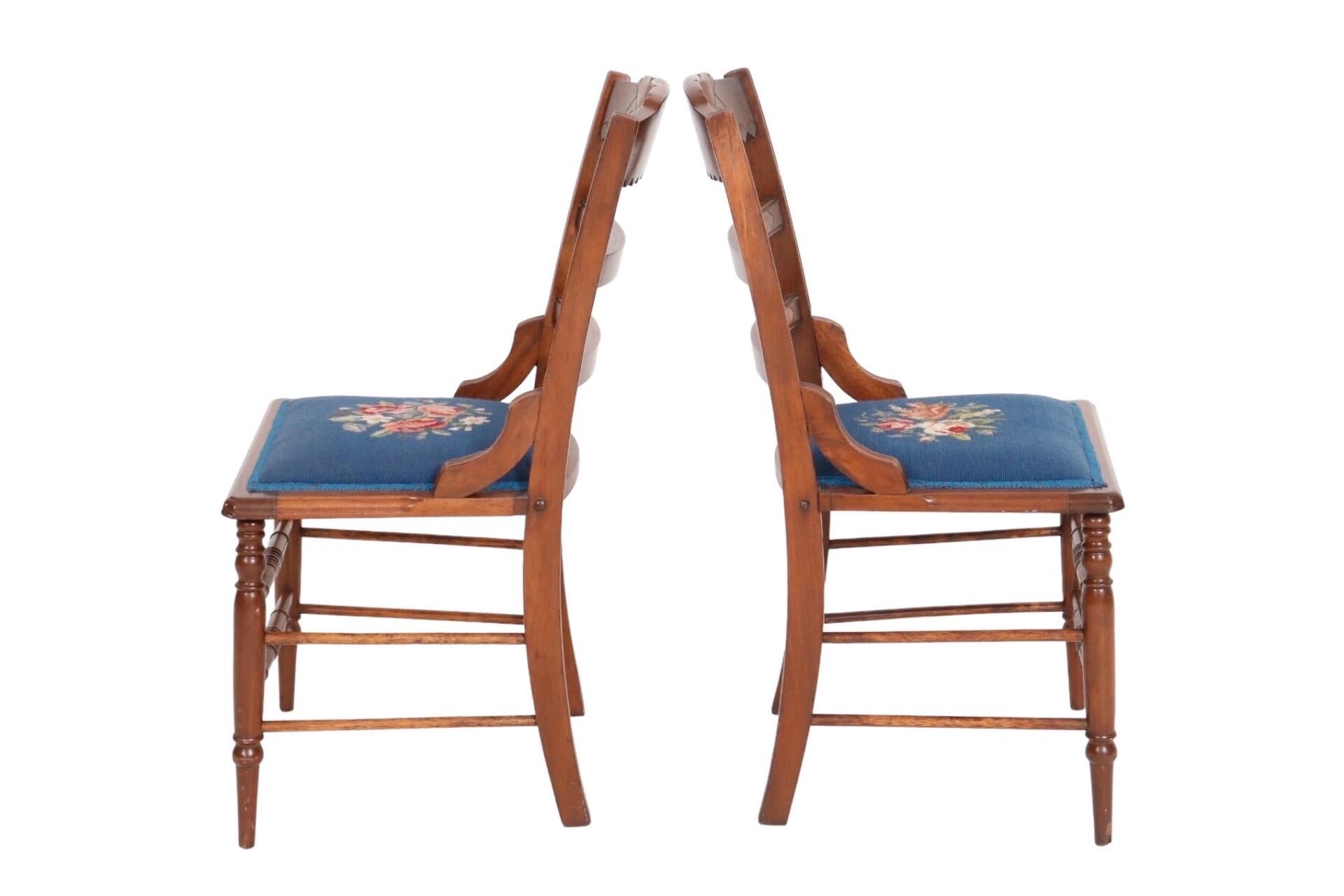 A pair of carved Eastlake period side chairs with needlepoint upholstered seats. The crest rail is decorated with birdseye maple and a square motif with beveled concentric circles. Turned legs are connected with a double box stretcher. The seat