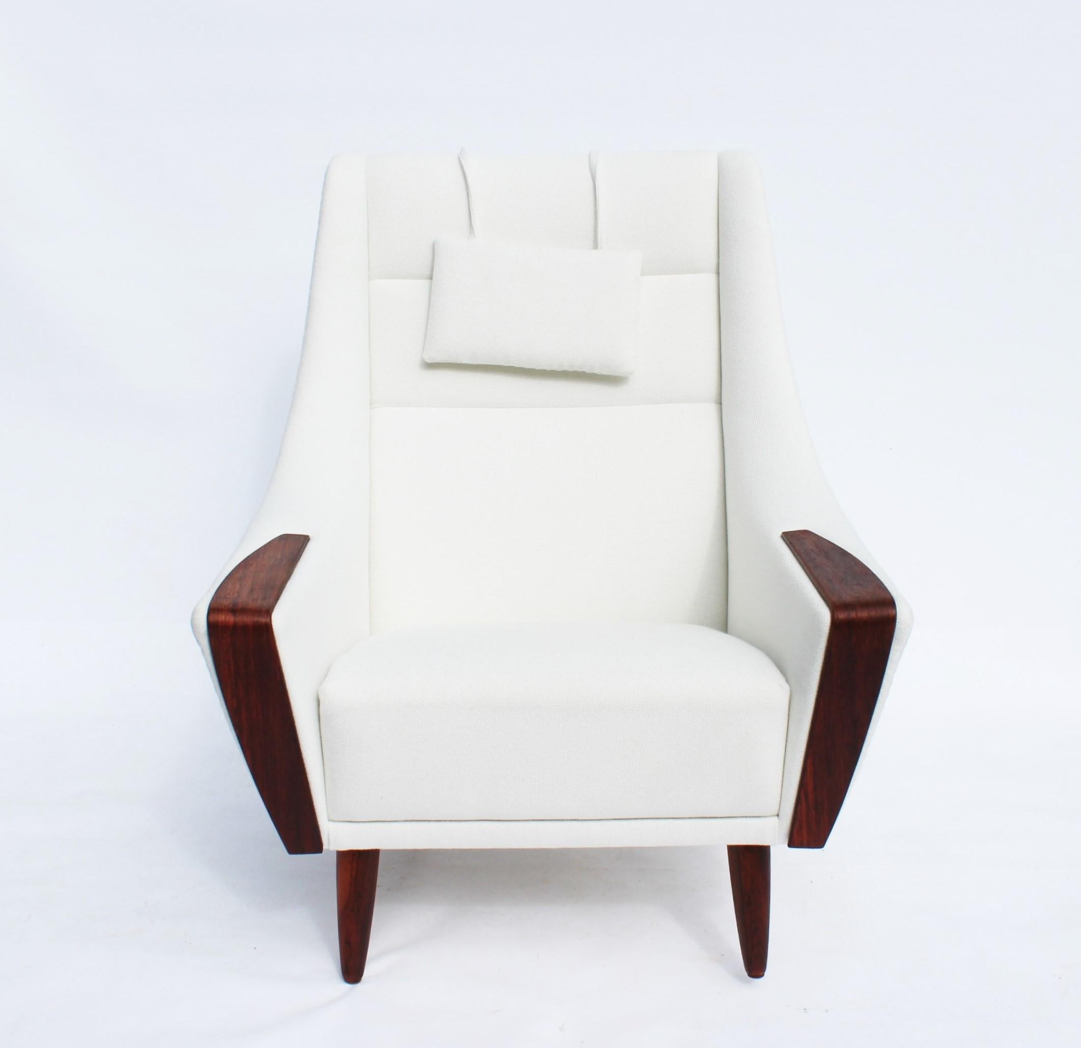 Le fauteuil à haut dossier, magnifiquement tapissé de tissu blanc et reposant élégamment sur des pieds en bois de rose, représente une pièce emblématique du design danois des années 1960. Méticuleusement restaurée et retapissée, cette chaise est