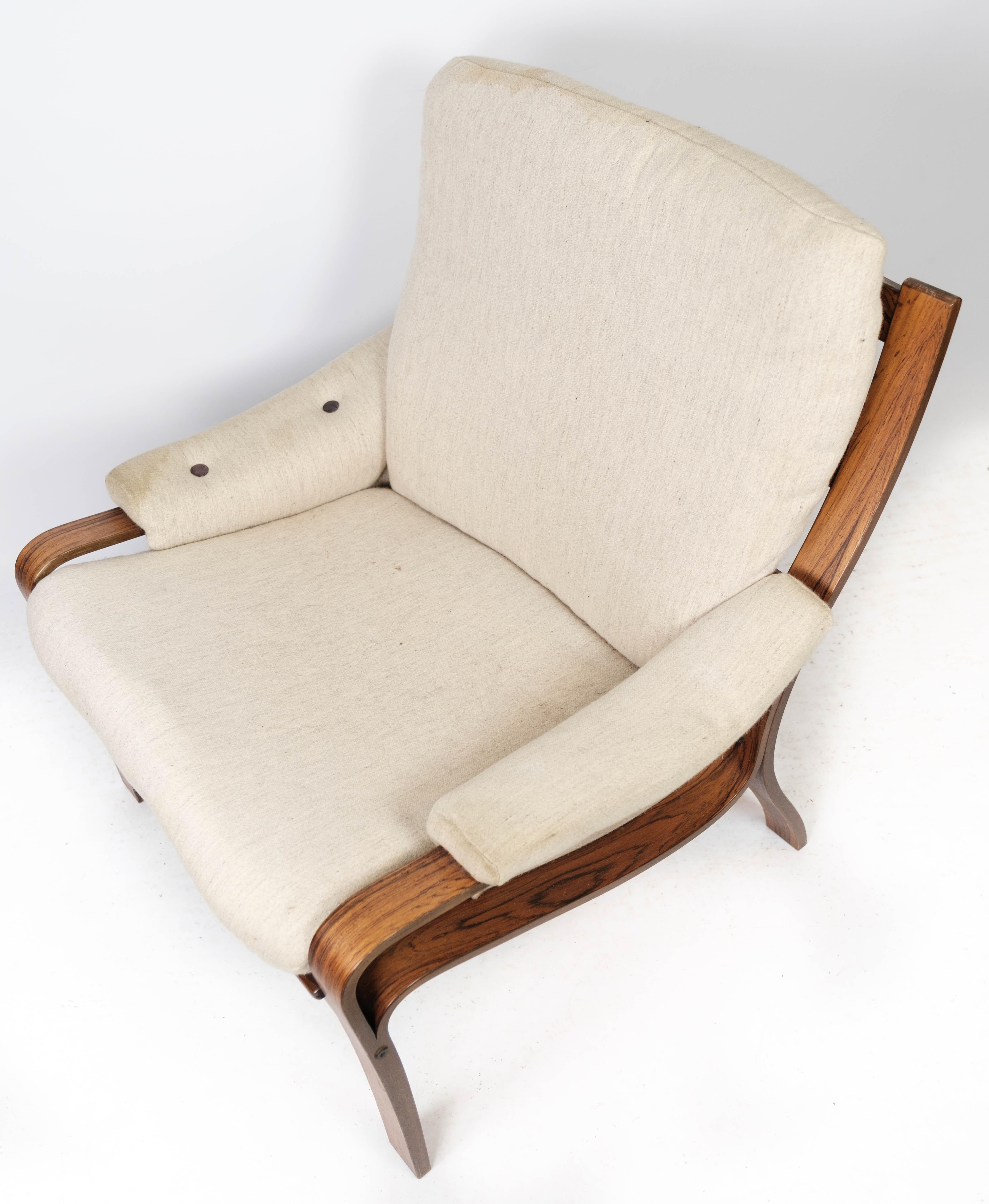Der mit hellem Stoff bezogene Sessel aus Palisanderholz im dänischen Design der 1960er Jahre ist ein elegantes und bequemes Möbelstück, das zeitlose Schönheit und Handwerkskunst ausstrahlt.

Die warmen Farbtöne und das schöne natürliche Muster des