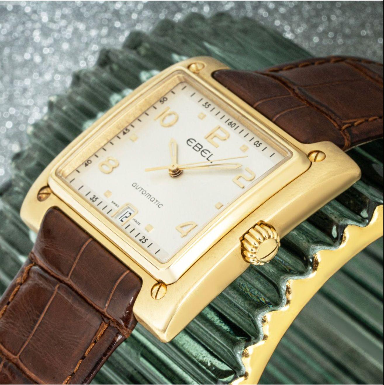 A mens yellow gold Ebell 1911 La Carre. Featuring a silver dial with applied arabic numbers, a date aperture and a yellow gold bezel. Fitted with a sapphire glass, a self-winding automatic movement and an Ebel brown leather strap equipped with an