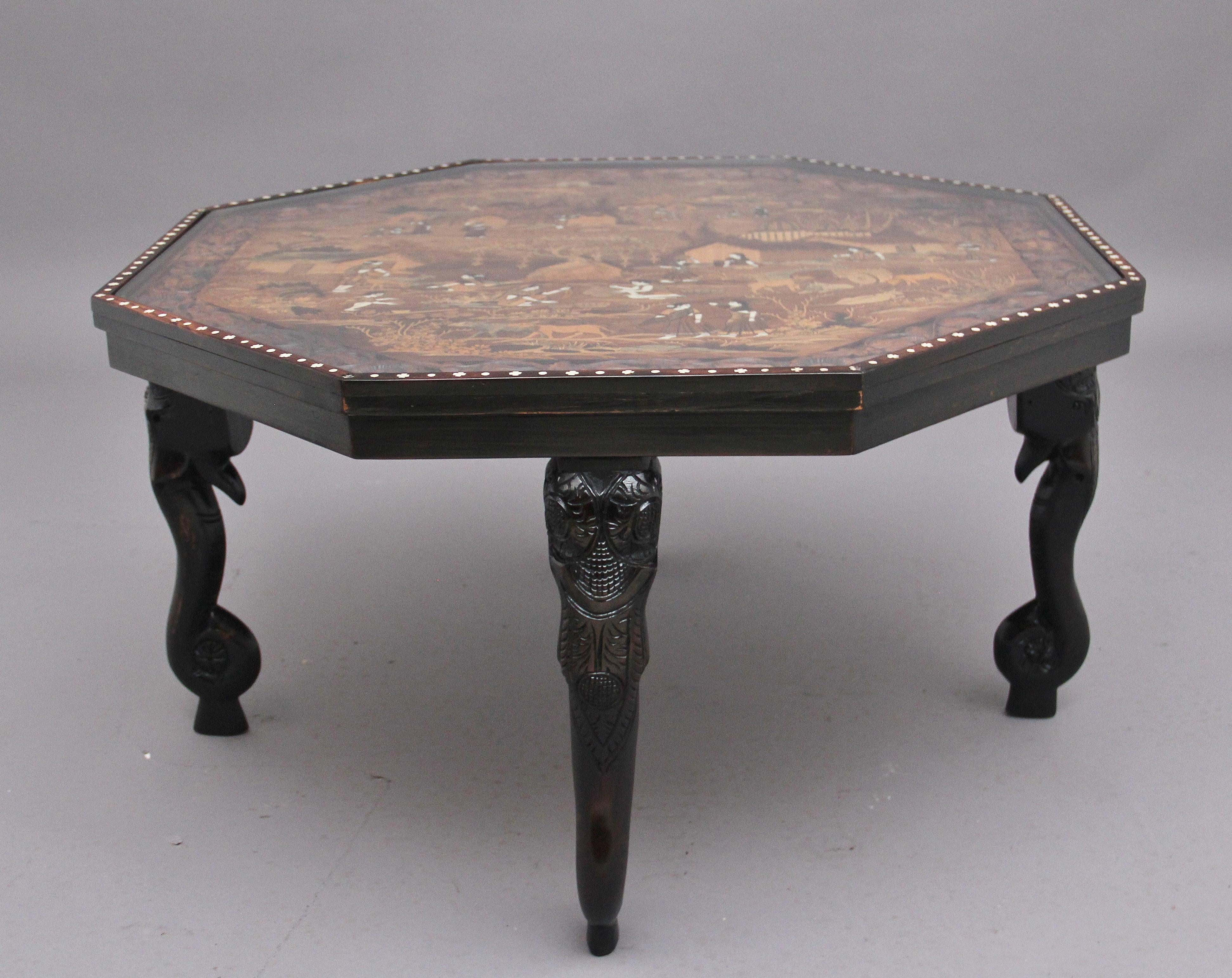 Table d'appoint / table basse indienne en ébène, très décorative, datant du milieu du 20e siècle. Le plateau de forme octogonale est richement incrusté d'une scène de campagne indienne et présente une bordure sculptée de fleurs, le plateau est