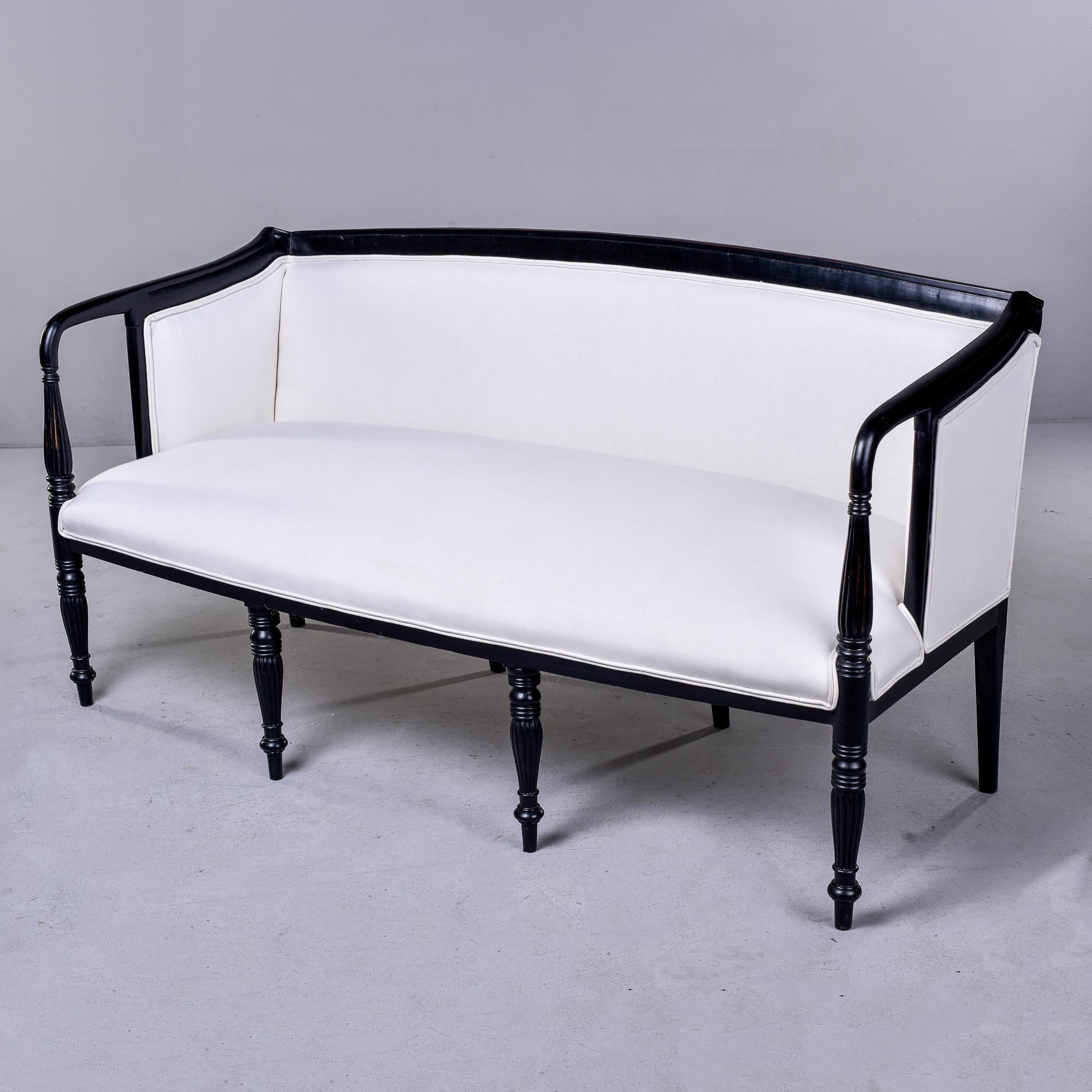 Trouvé en Angleterre, ce canapé ou sofa des années 1920 a un cadre récemment ébénisé et est recouvert de mousseline blanche - prêt à être tapissé dans le tissu de votre choix. La structure à huit pieds présente des détails tournés et anglés et des