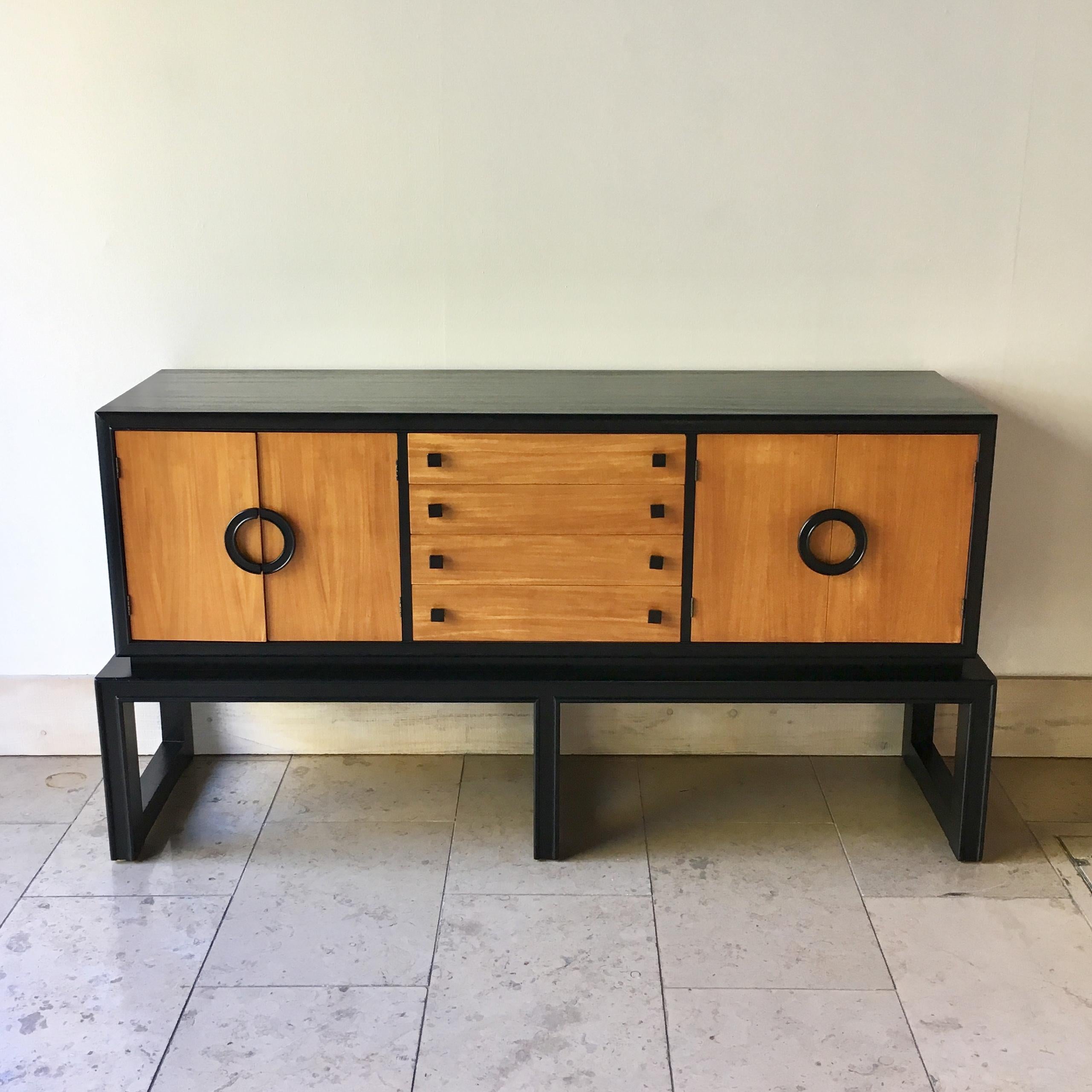 Wooden cabinet with ebonised surfaces and edges on an ebonised raised three legged plinth. The semi circle handles and square handles are ebonised. The cabinet had 2 pairs of doors flanking four drawers and is made by Americraft, 1970s.
The makers
