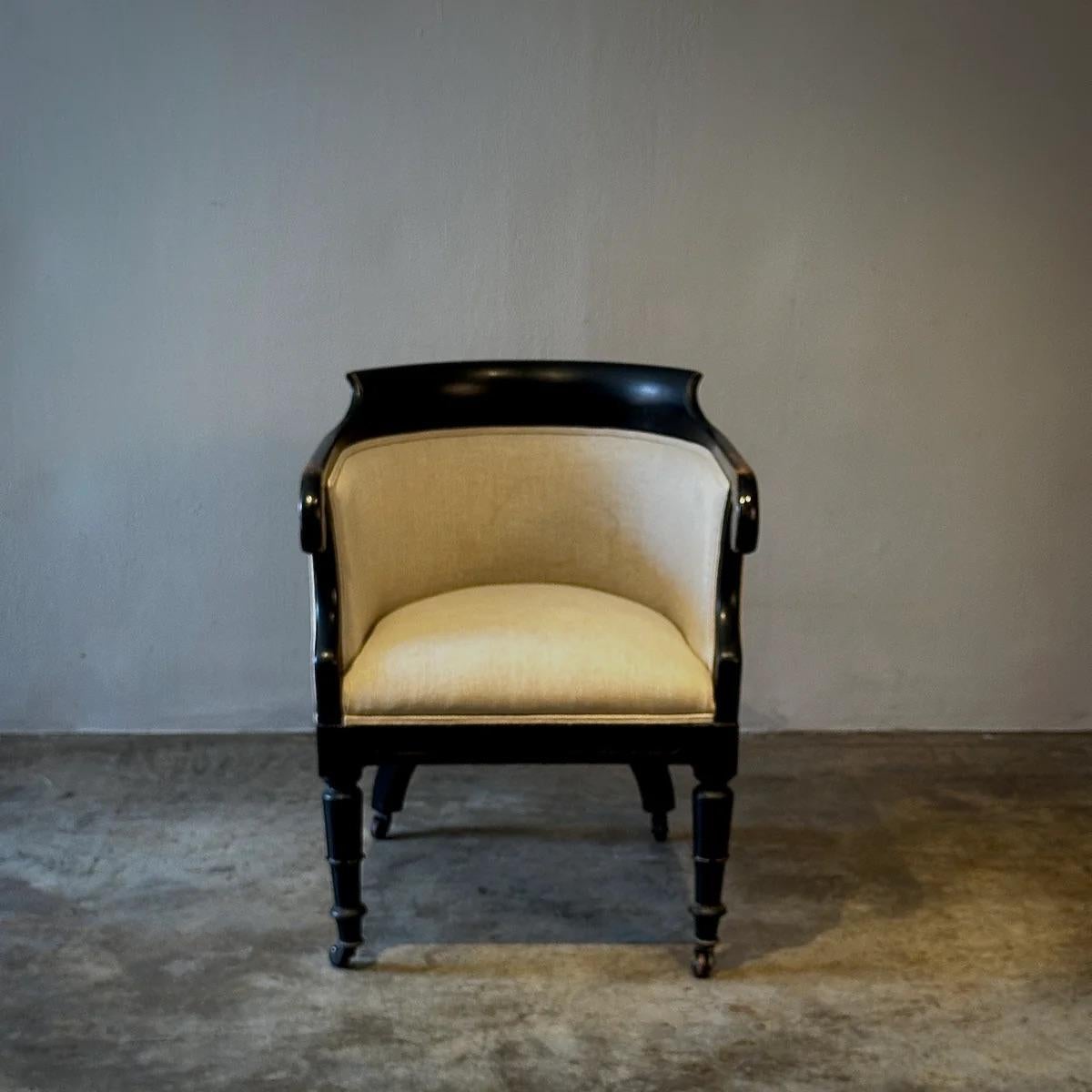 Esta exquisita silla de bañera ebonizada Jorge IV ejemplifica la elegancia clásica con su profundo acabado lacado en negro y su sutil curvatura. El robusto pero refinado armazón de la silla presenta brazos con elegantes volutas y patas estriadas