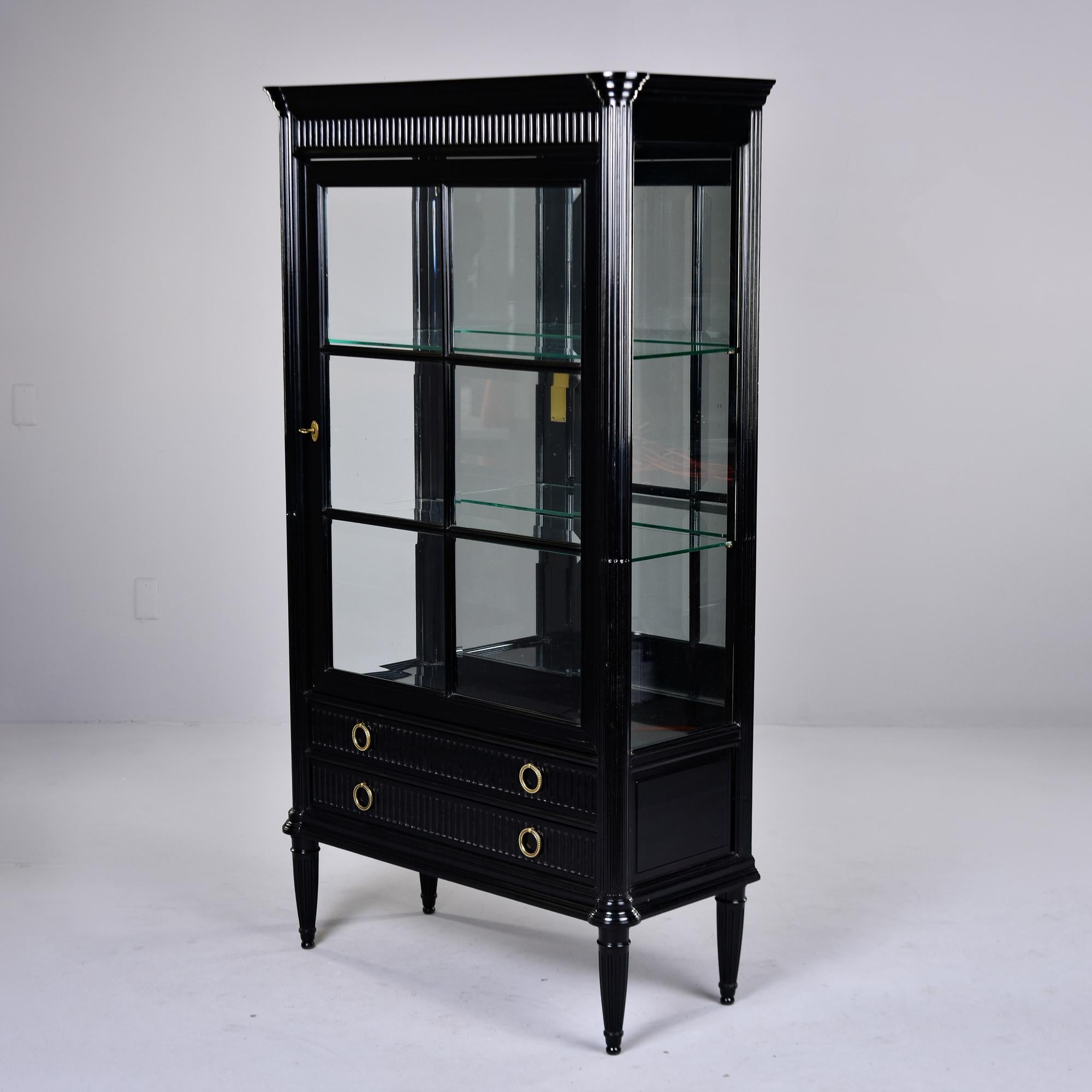 Found in France, this Louis Philippe style glass-front cabinet dates from the 1920s. New, professionally applied ebonised finish. Cabinet has pediment and reeded pilasters. Functional lock on door, two internal glass shelves and mirrored back.