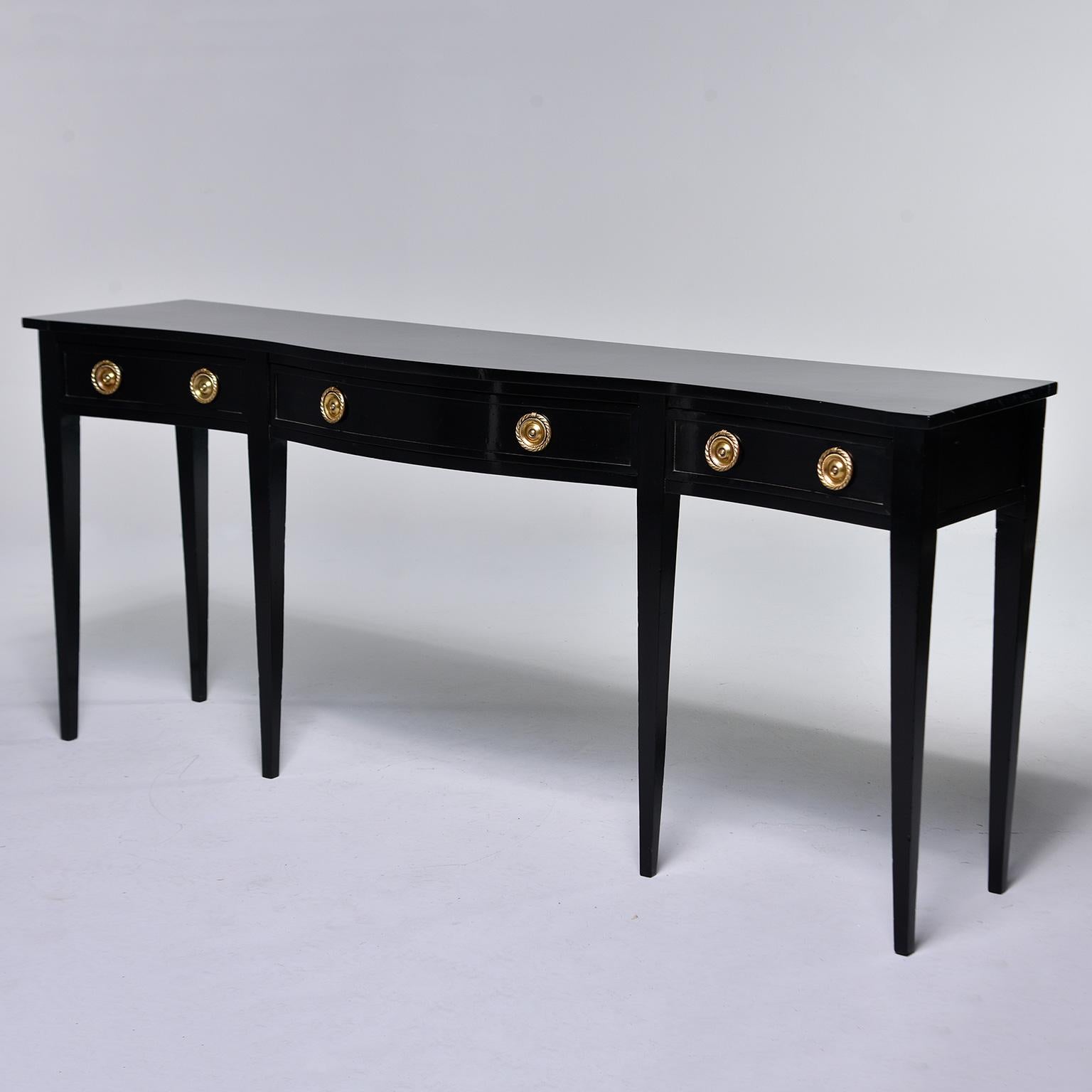 English six-legged mahogany console has a new ebonised finish, circa 1920s. Console has a graceful, curvy serpentine front, three functional drawers, brass hardware and slender, tapered legs. Unknown maker.