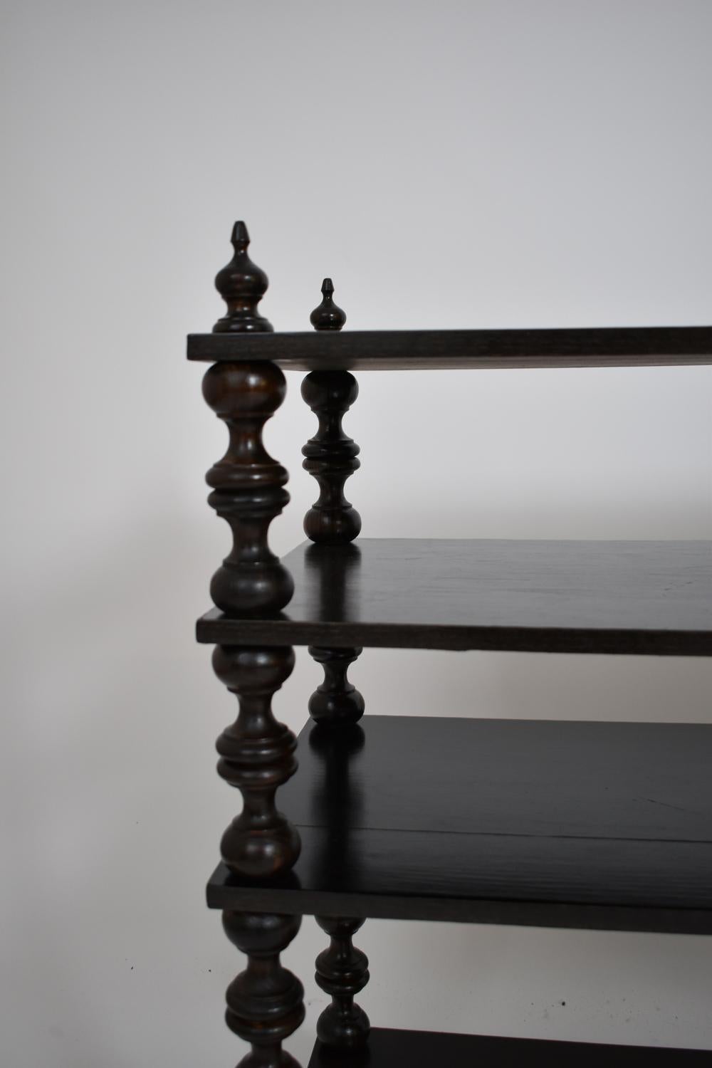 Consola librería de madera torneada ebonizada que descansa sobre cuatro patas que sostienen cuatro estantes. España, años 50.