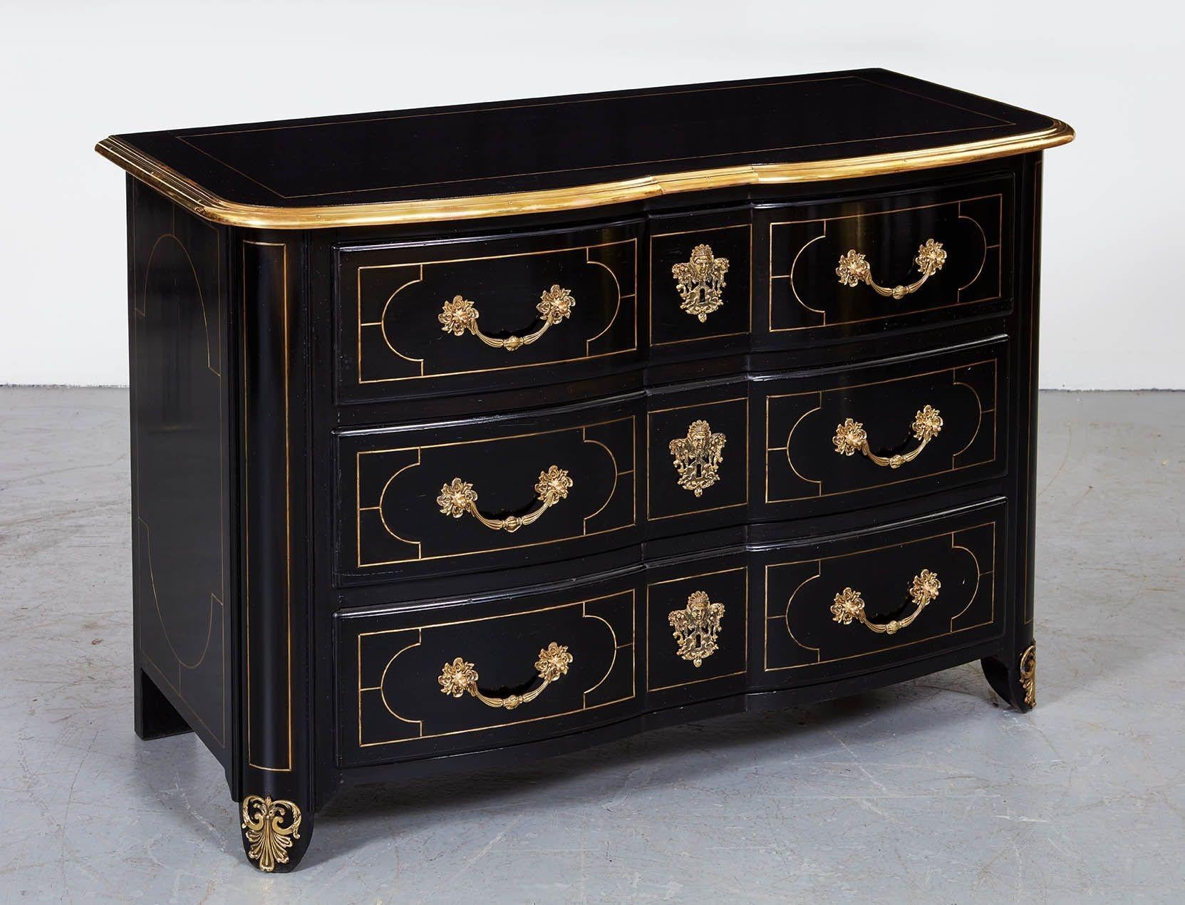 Ebonized and brass inlaid commode having shaped top with brass molded edge over three shaped drawers with brass string inlay and gilt bronze hardware and standing on straight molded and bronze mounted feet.
