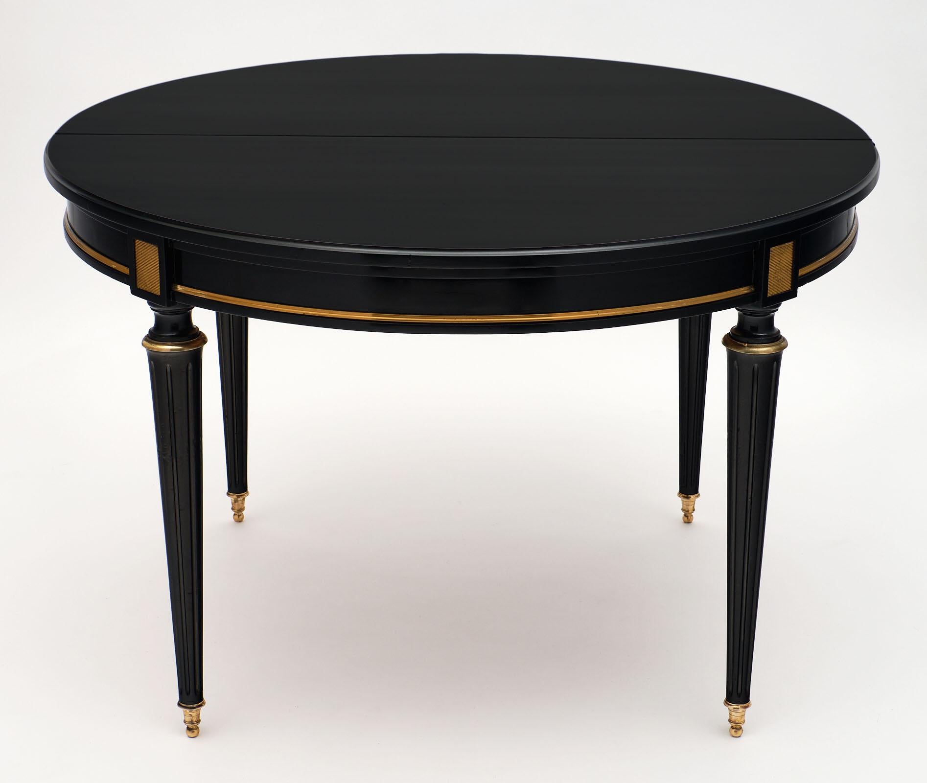Antique ebonized dining table with leaves made of solid mahogany and featuring gold brass trims. We love the round shape that expands with leaves, and the tapered and fluted legs. The feet are capped with bronze, a classic accent of the Louis XVI
