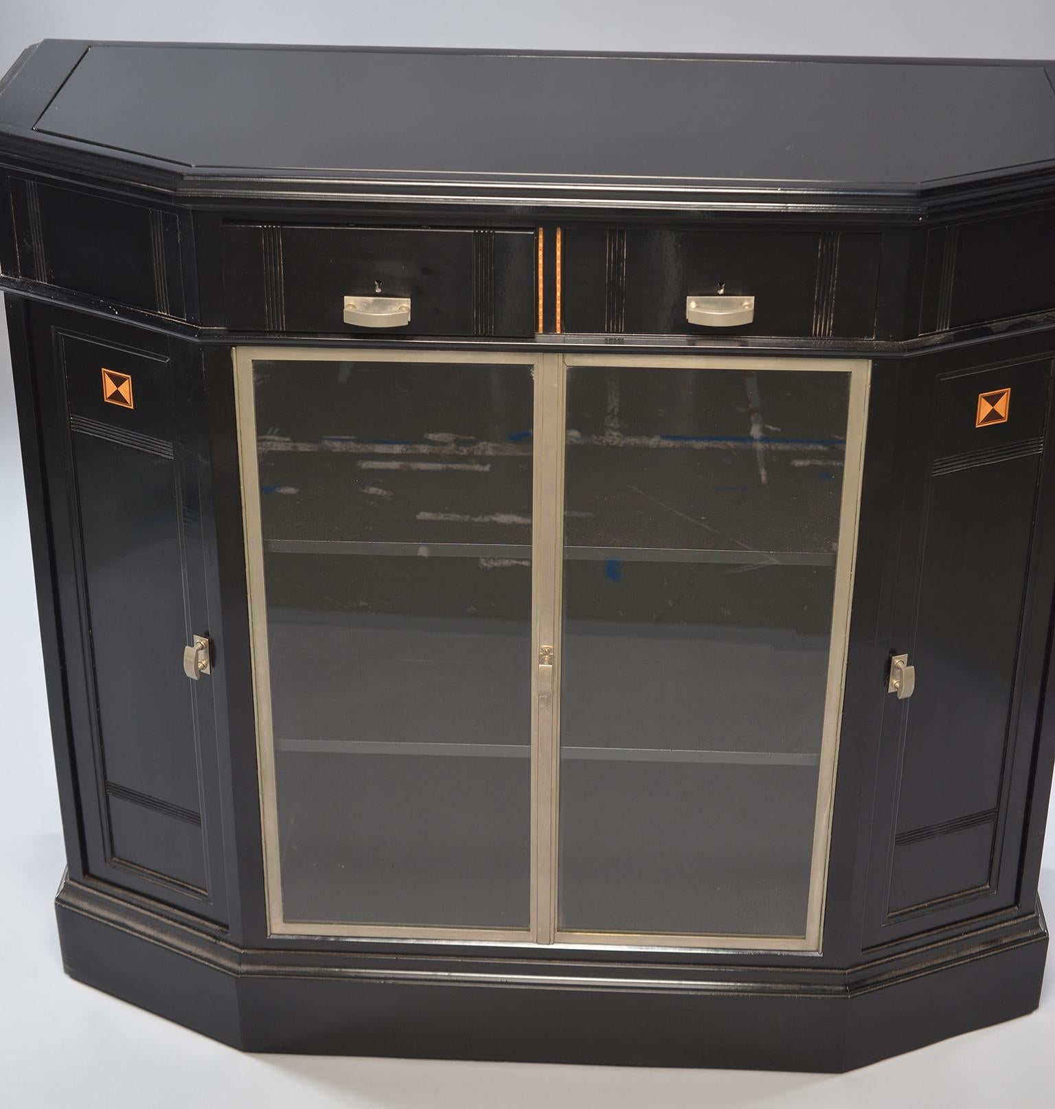 Art Deco cabinet found in Belgium, circa 1930s. New ebonized finish with lower center glass front doors, decorative aluminum trim. Center glass doors are flanked by side cabinets set on an angle with interior shelves and there are two small drawers