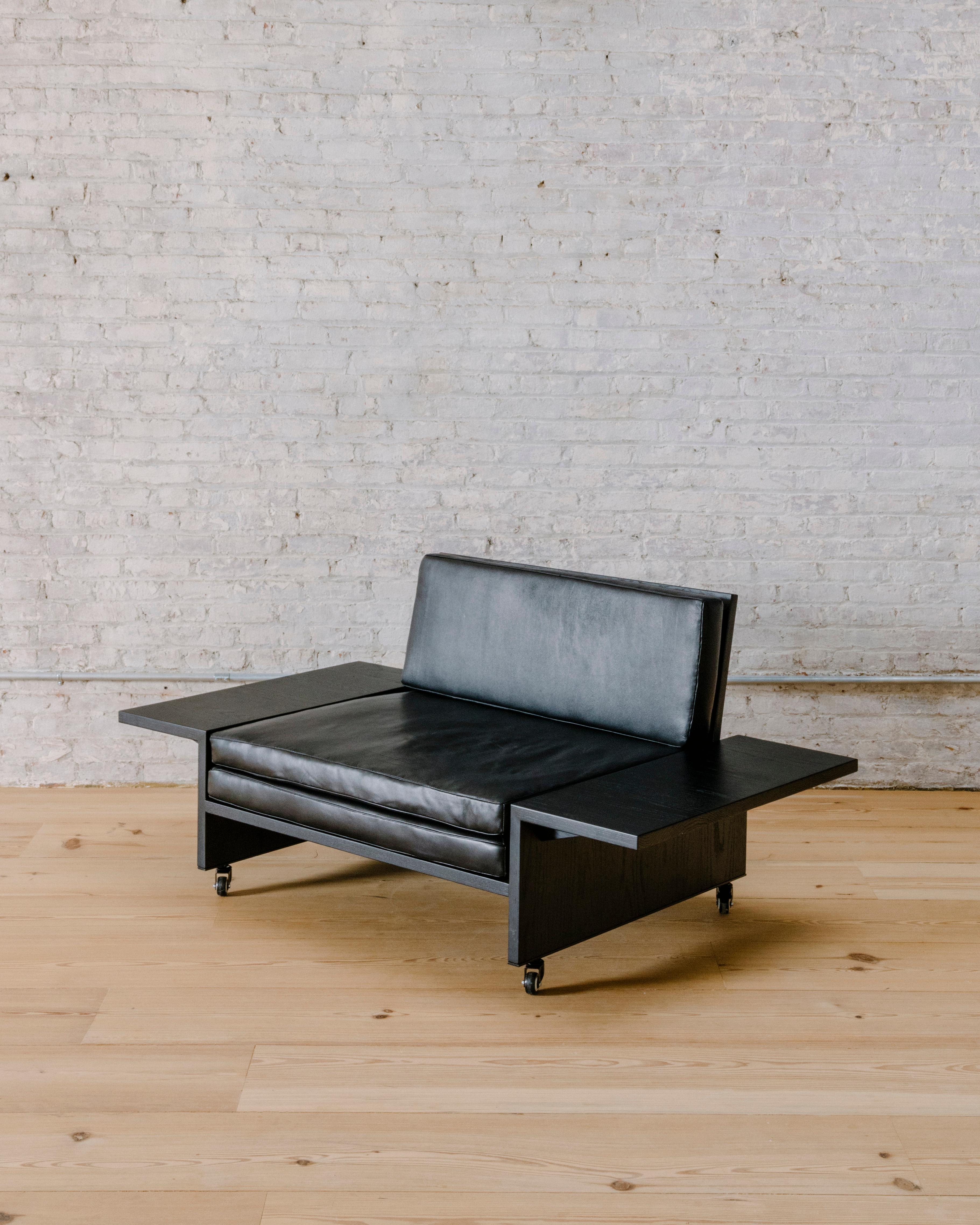 Constructed from charred ash boards, the minimal Domino armchair by Brooklyn-based Mock Studio rethinks the idea of an armrest as side table. Low and loungey, mounted on wheels and wide enough to call itself a love seat, this piece belongs in a