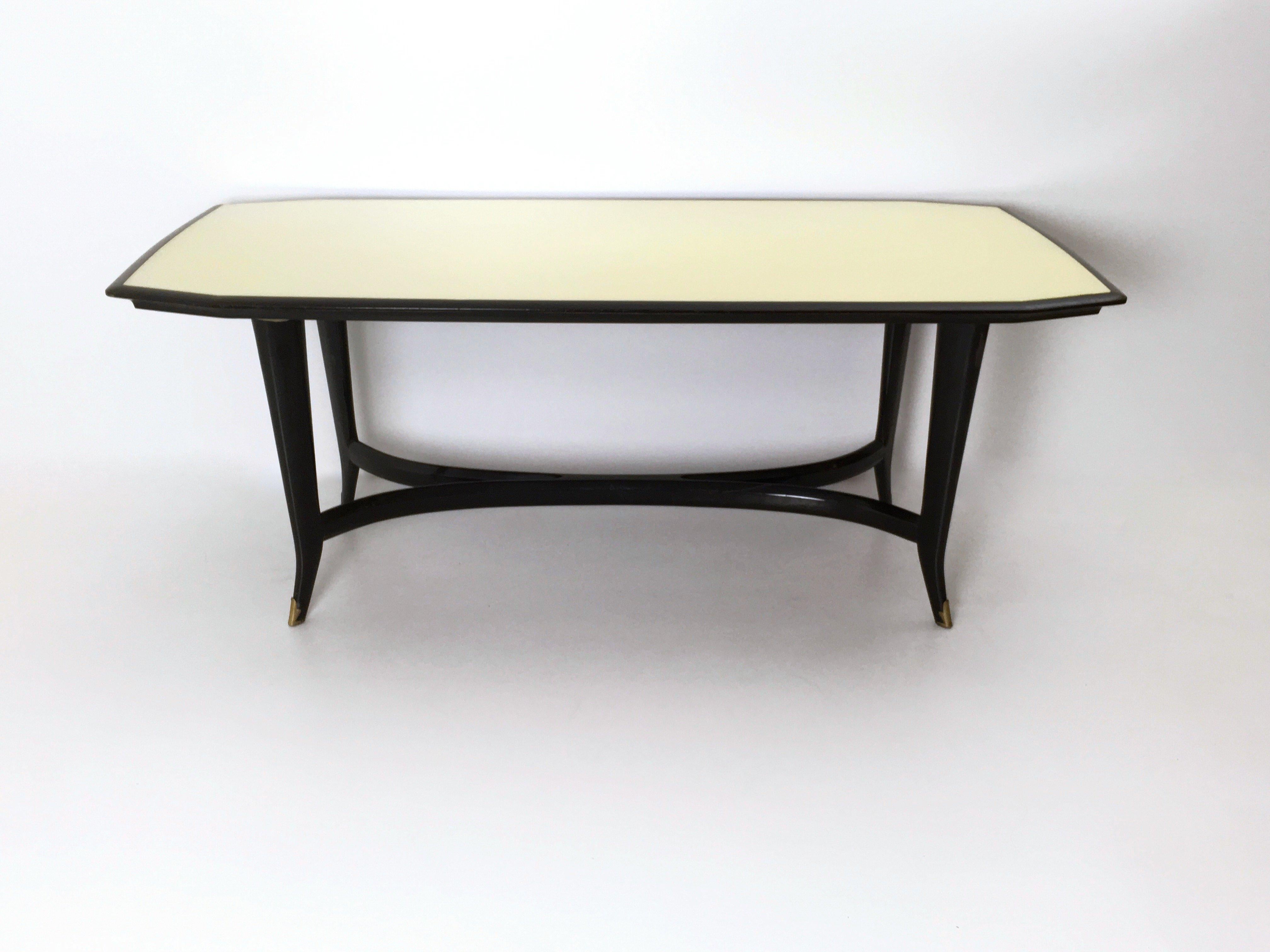 1950s.
It is made in ebonized beech and features a back-painted glass top and brass feet caps. 
It may show slight traces of use since it's vintage, but it can be considered as in excellent original condition and ready to become a piece in a