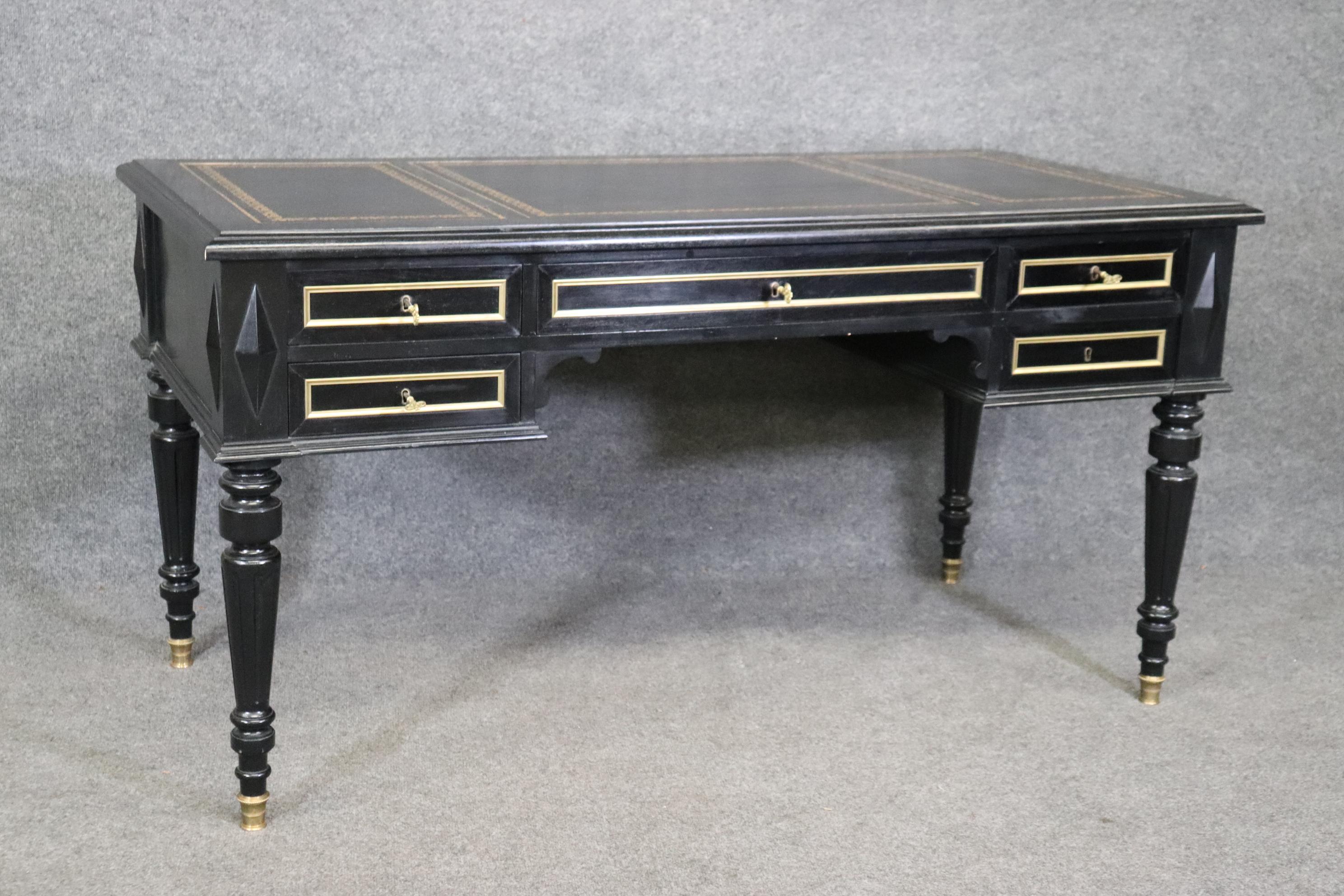 This is a gorgeous Baker quality brass trimmed desk with a wonderful gold embossed and tooled leather top. The desk is ebonized in black lacquer and features remarkable build quality and superb details in brass such as trim durrounding each of the 5