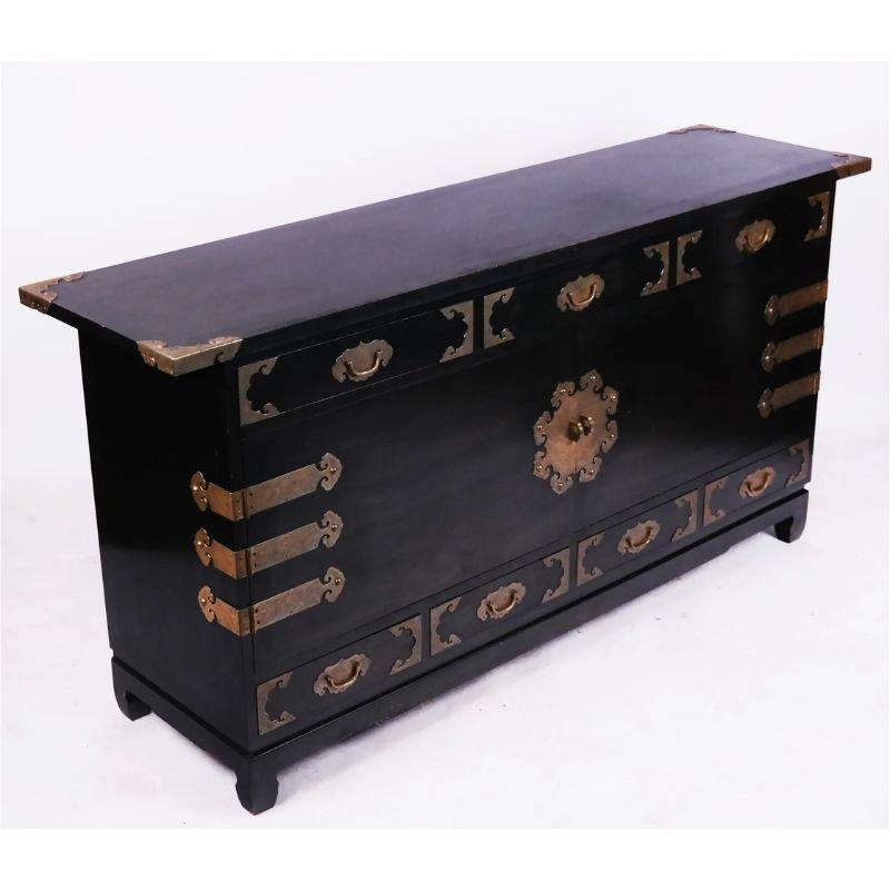 An ebonized Chinese sideboard with brass fittings.  The black top extends beyond the frame of the cabinet and each corner has a distinctive brass detail with etching typical of Asian style.  The center of the cabinet is highlighted with round brass
