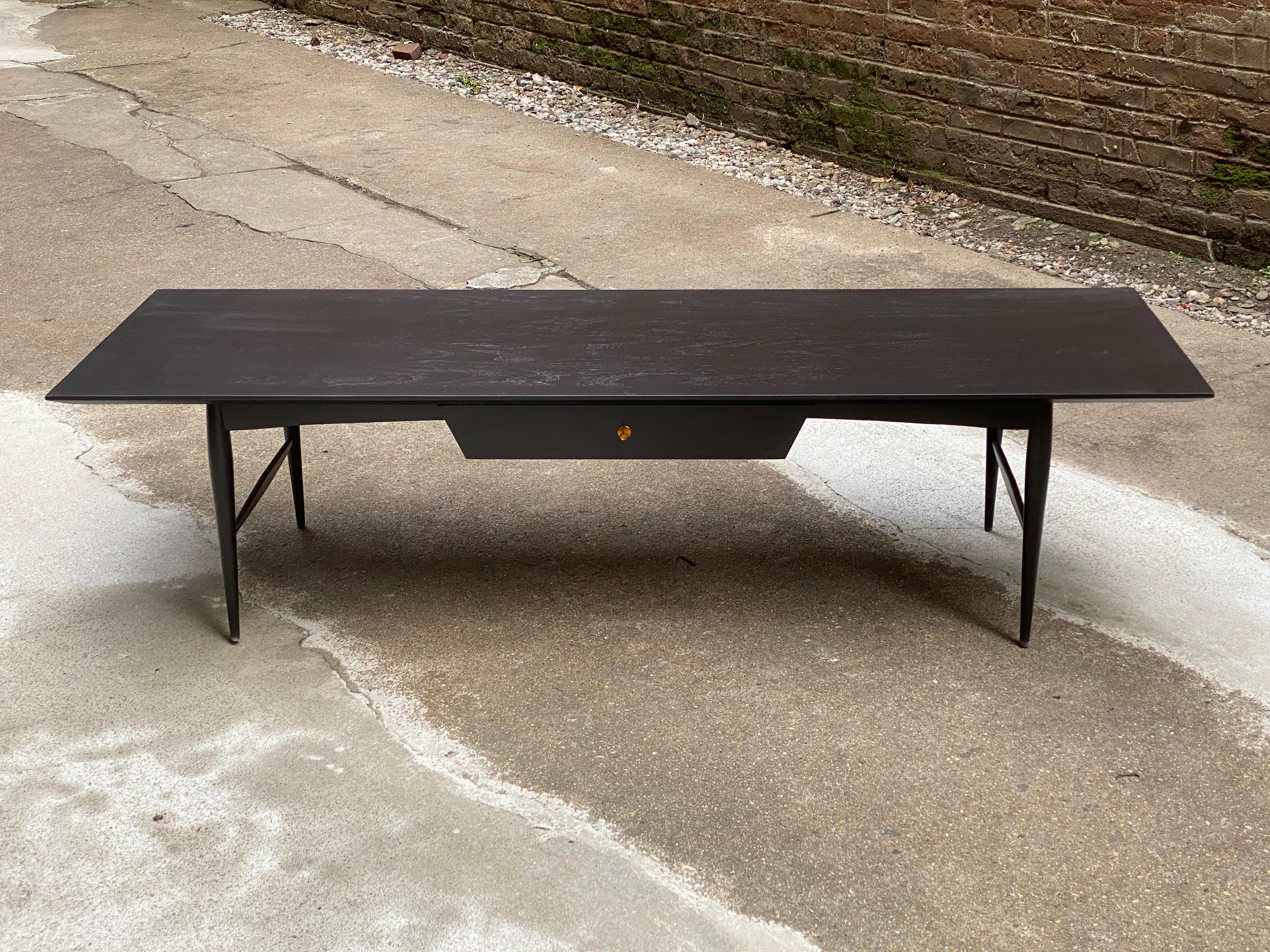 Large rectangular top ebonized finish coffee table with one drawer and one false front. Copper finished pulls. Elegant tapered legs and stretcher base, circa 1960. Very nice condition.

Approximately 60