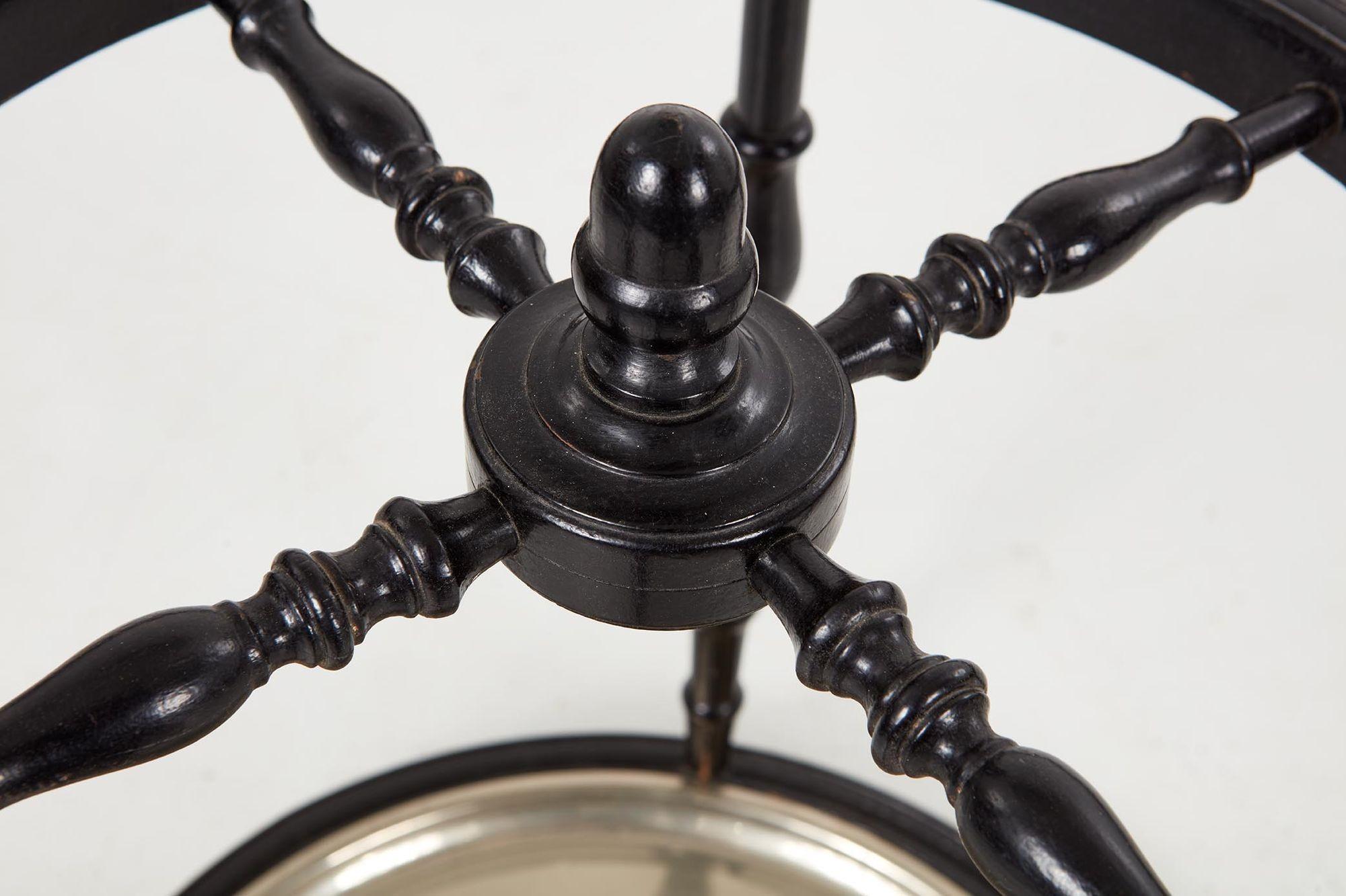 An ebonized umbrella stand with compass style top and base joined by turned legs and a top cross-stretcher with finial, having a silver plate circular drip pan. A graphic nautical design. Useful in a boot room or entry hall.