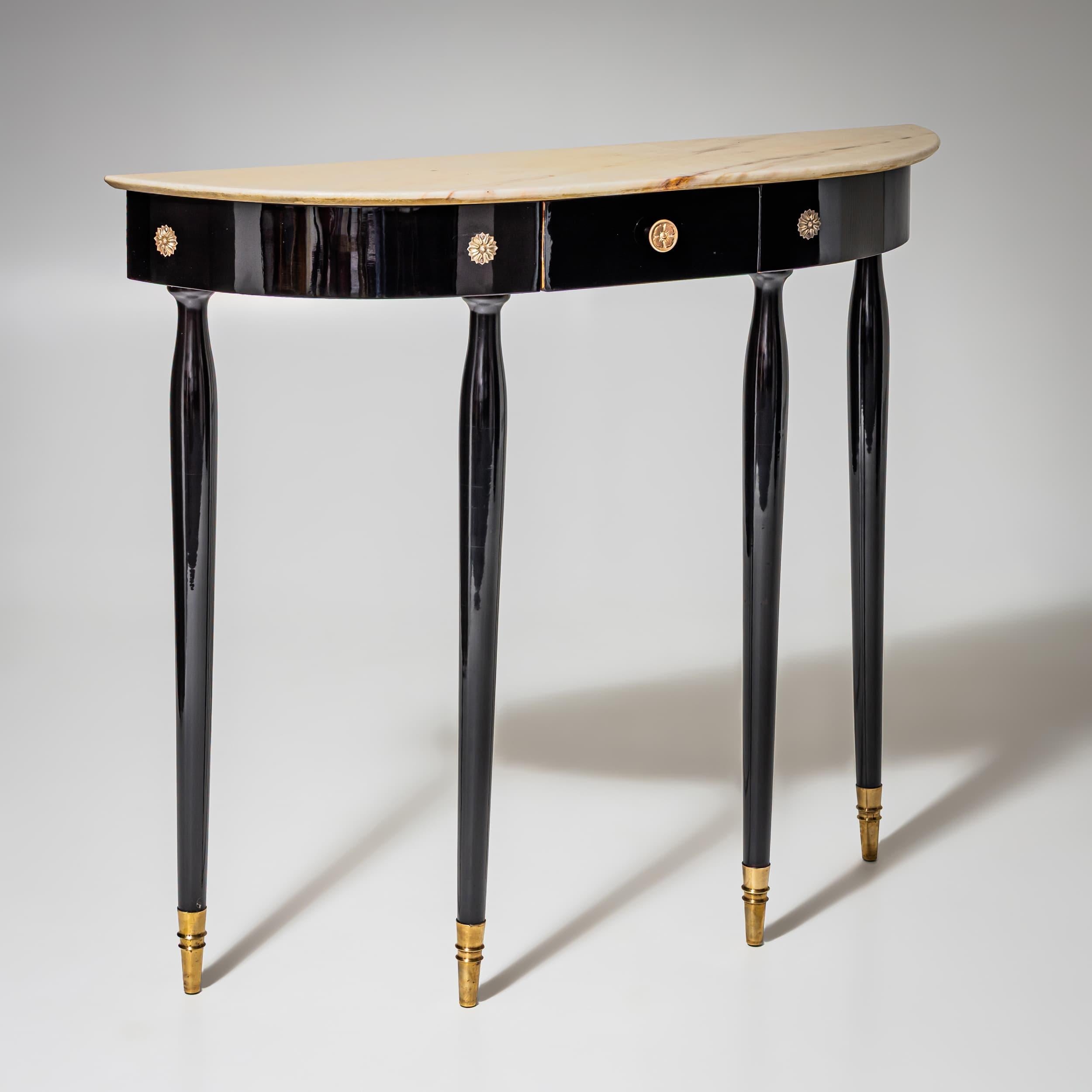 Ebonized demi-lune console table with four tapered legs, brass sabots, and rosette mounts on the apron. A drawer is integrated into the apron. The tabletop features a beige onyx slab. Restored and hand-polished.