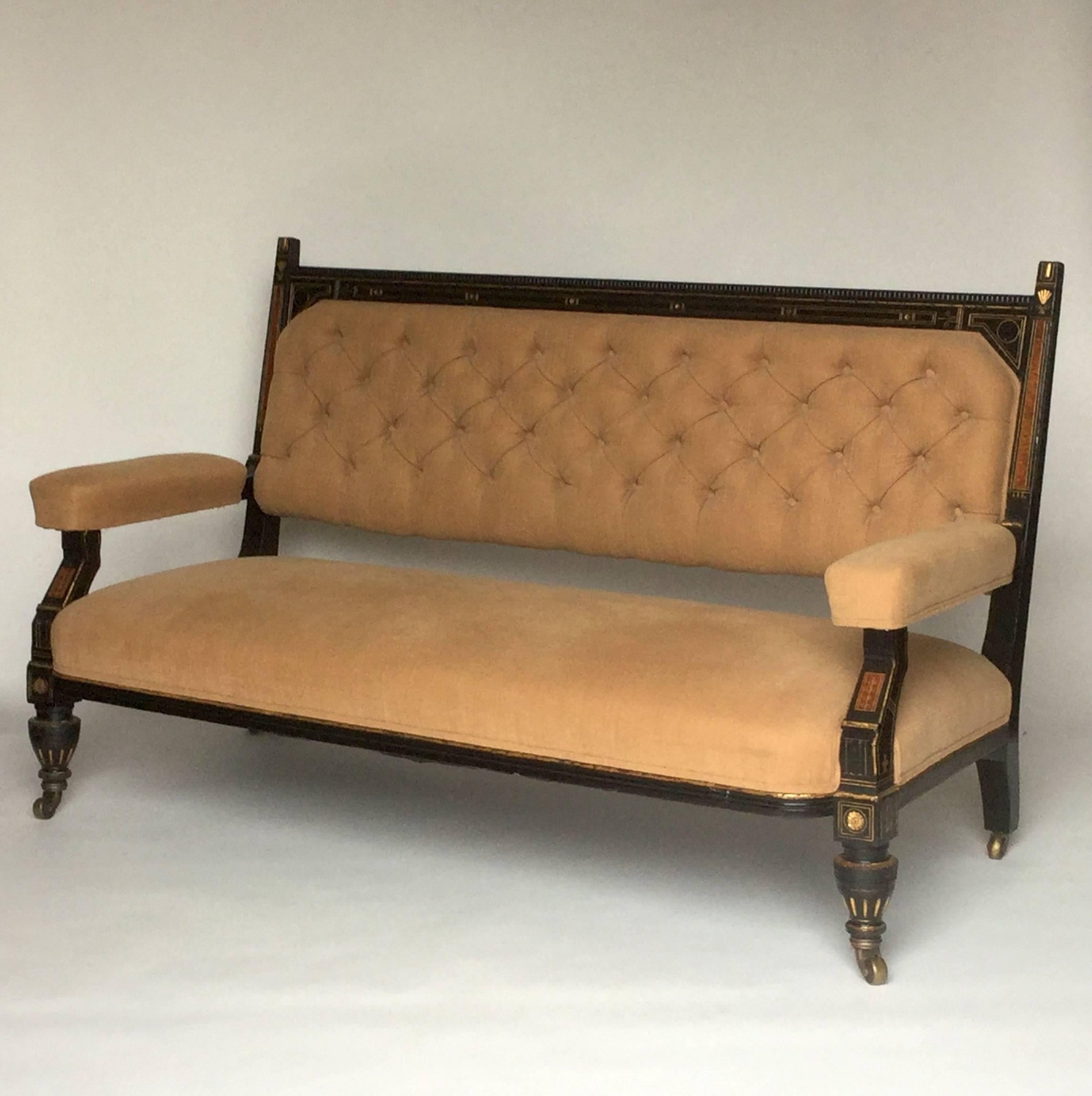 Very handsome ebonized Eastlake settee, circa 1890, ebonized oak with incised gold leaf detailing and faux bois burled wood inserts, upholstered in buff colored cotton velour with padded armrests, button tufted back with self covered buttons, brass