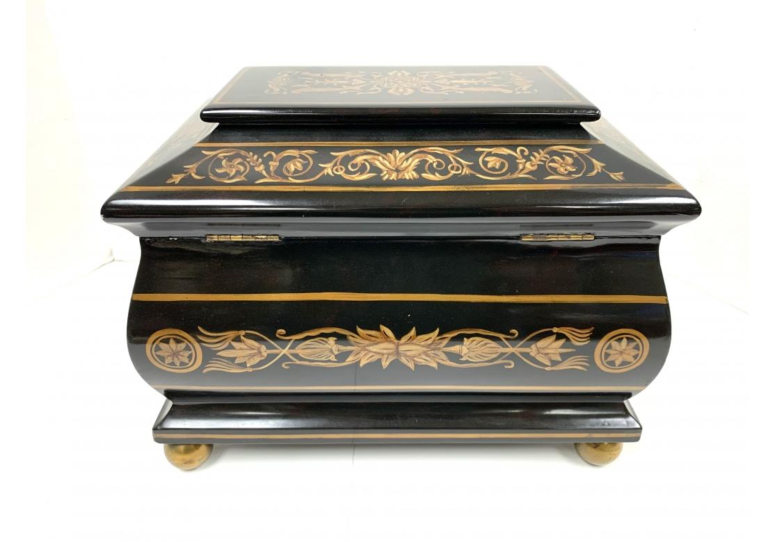 Ebonized footed wooden box with hinged lid and decorated with gold foliate and compass rose designs. The box having a sarcophagus form and resting on brass bun feet.
Dimensions: 12