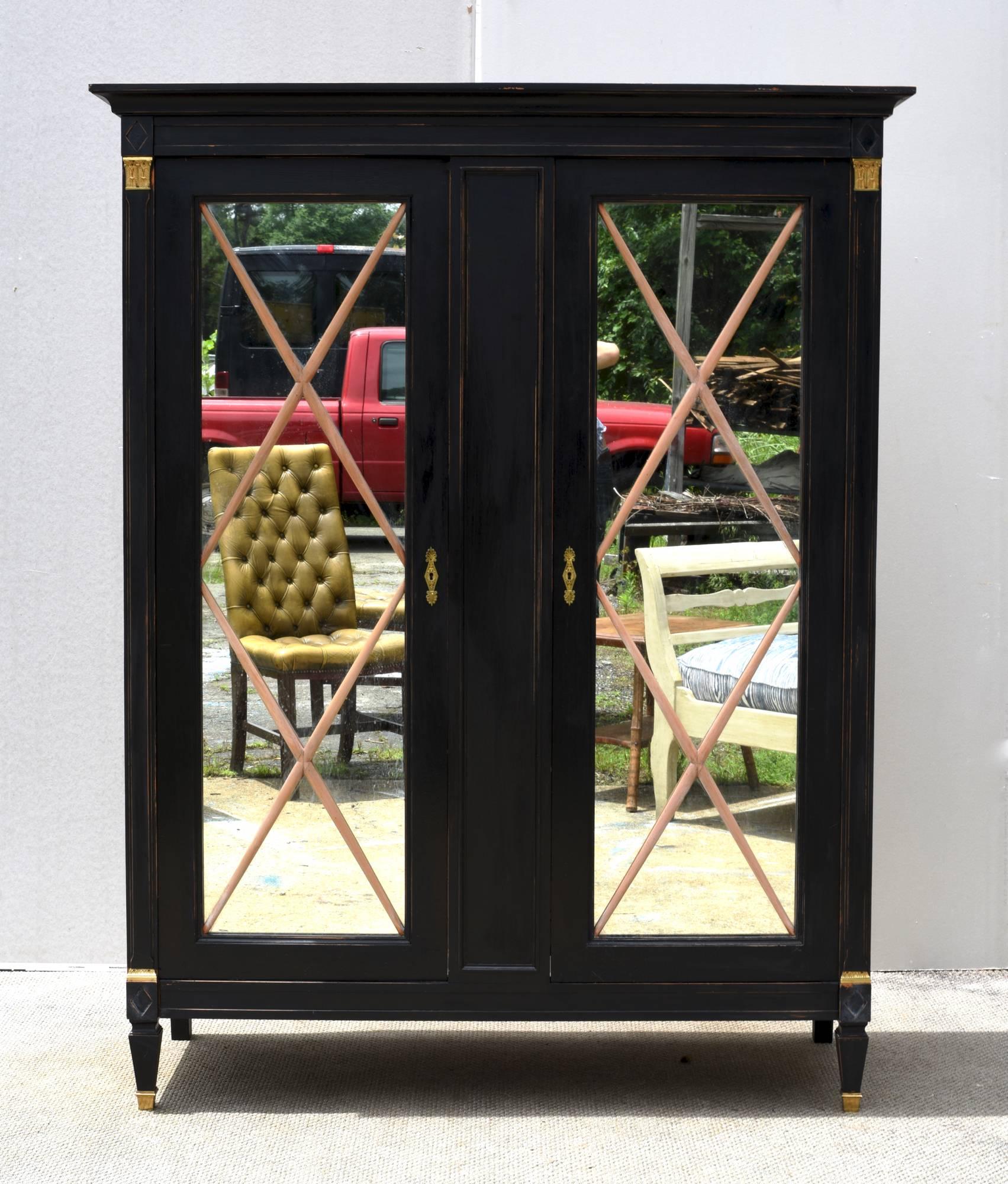 A handsome ebonized two door cabinet in the neoclassical taste having glamorous brass accents and hand bleached 