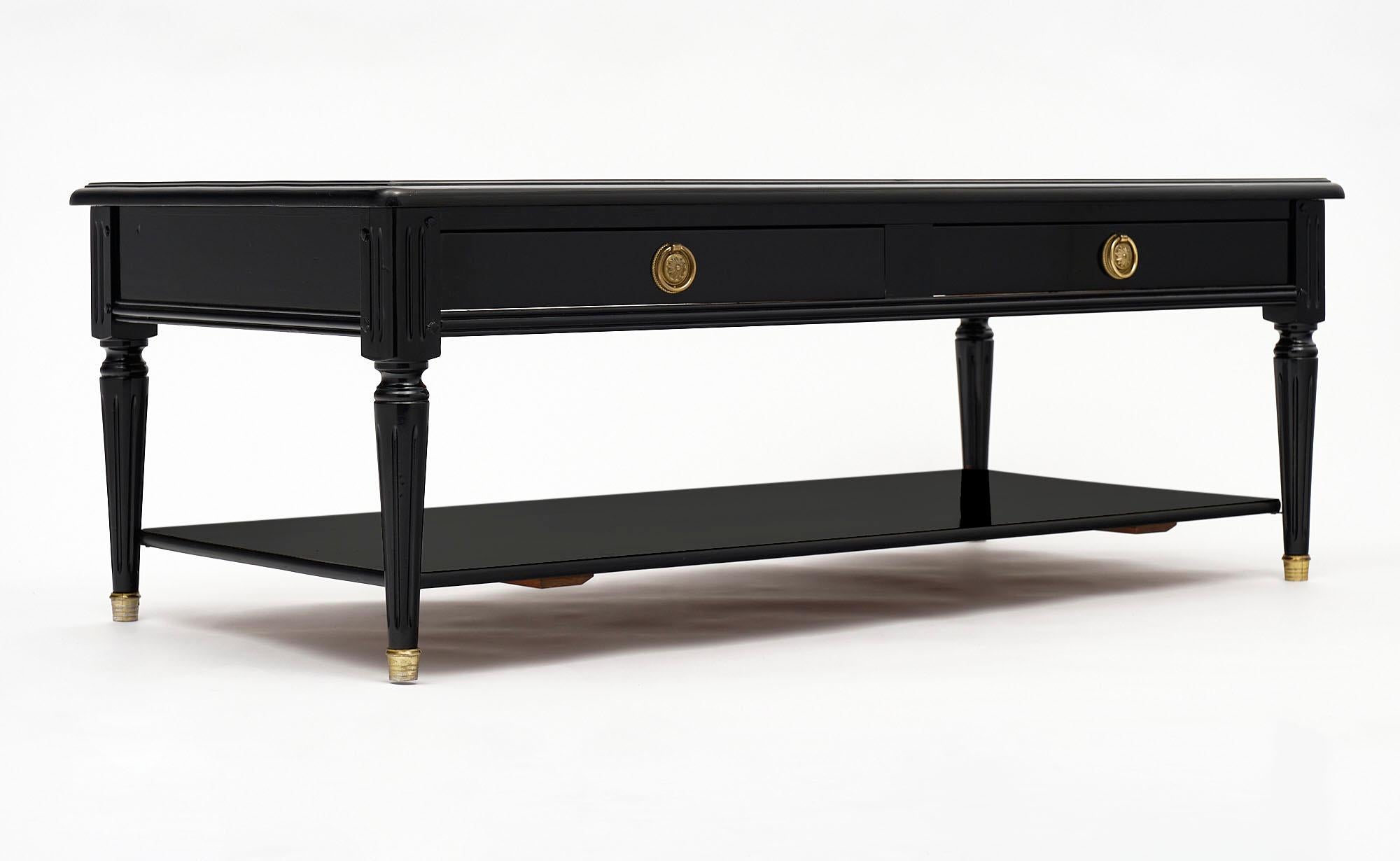 Ebonized French vintage coffee table in the Louis XVI style. This table has been ebonized and finished with a lustrous French polish. It features two drawers and a shelf. The gilt brass hardware are complimented by the capped feet.