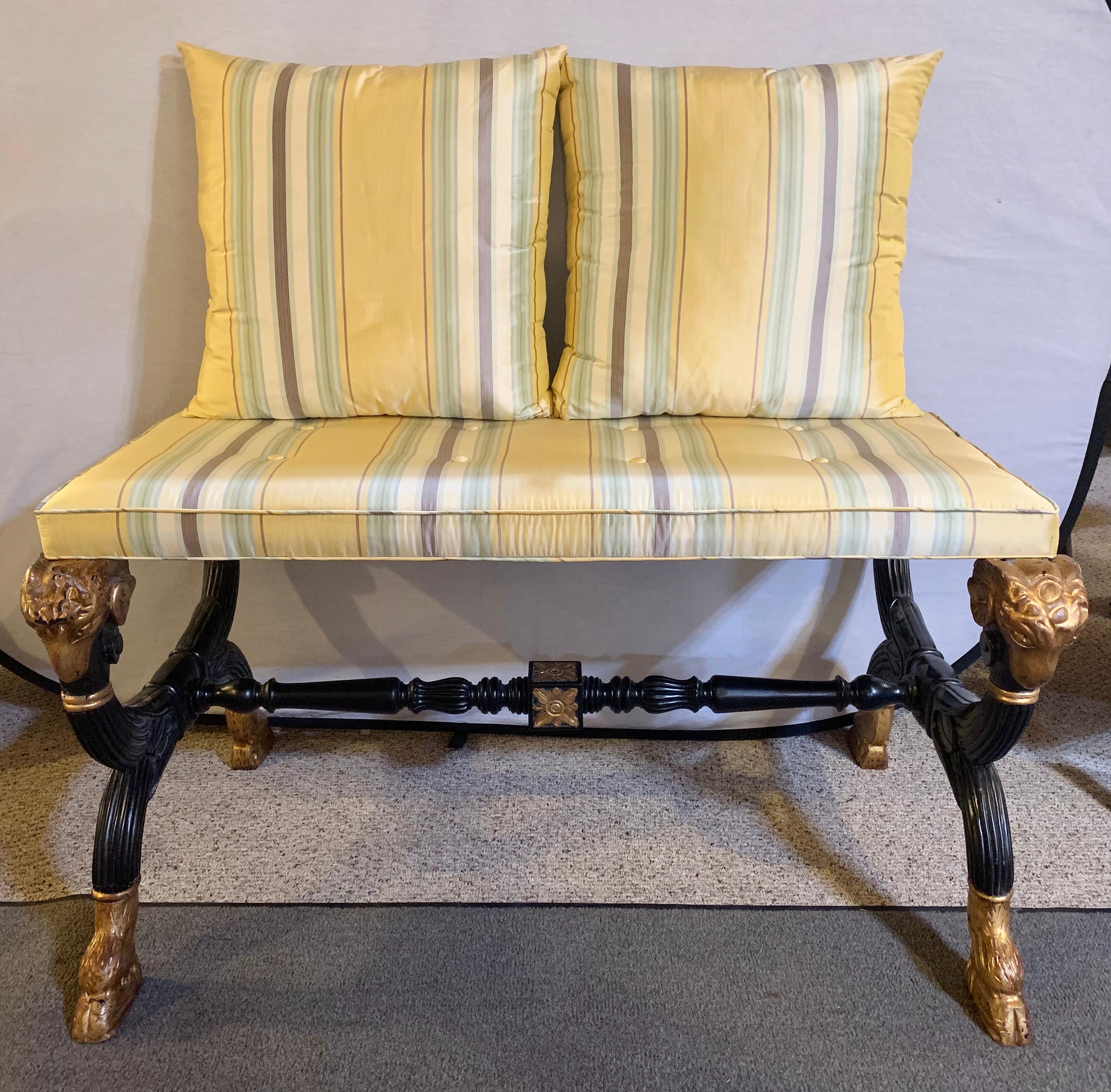 Ebonized & gilt benches or settes having mantra silk scalamandre upholstery. A fine pair each with a gilt rams head hand-rest. The pair of Hollywood Regency benches are simply stunning in their ebony finish with gilt carved hoof feet and rams heads