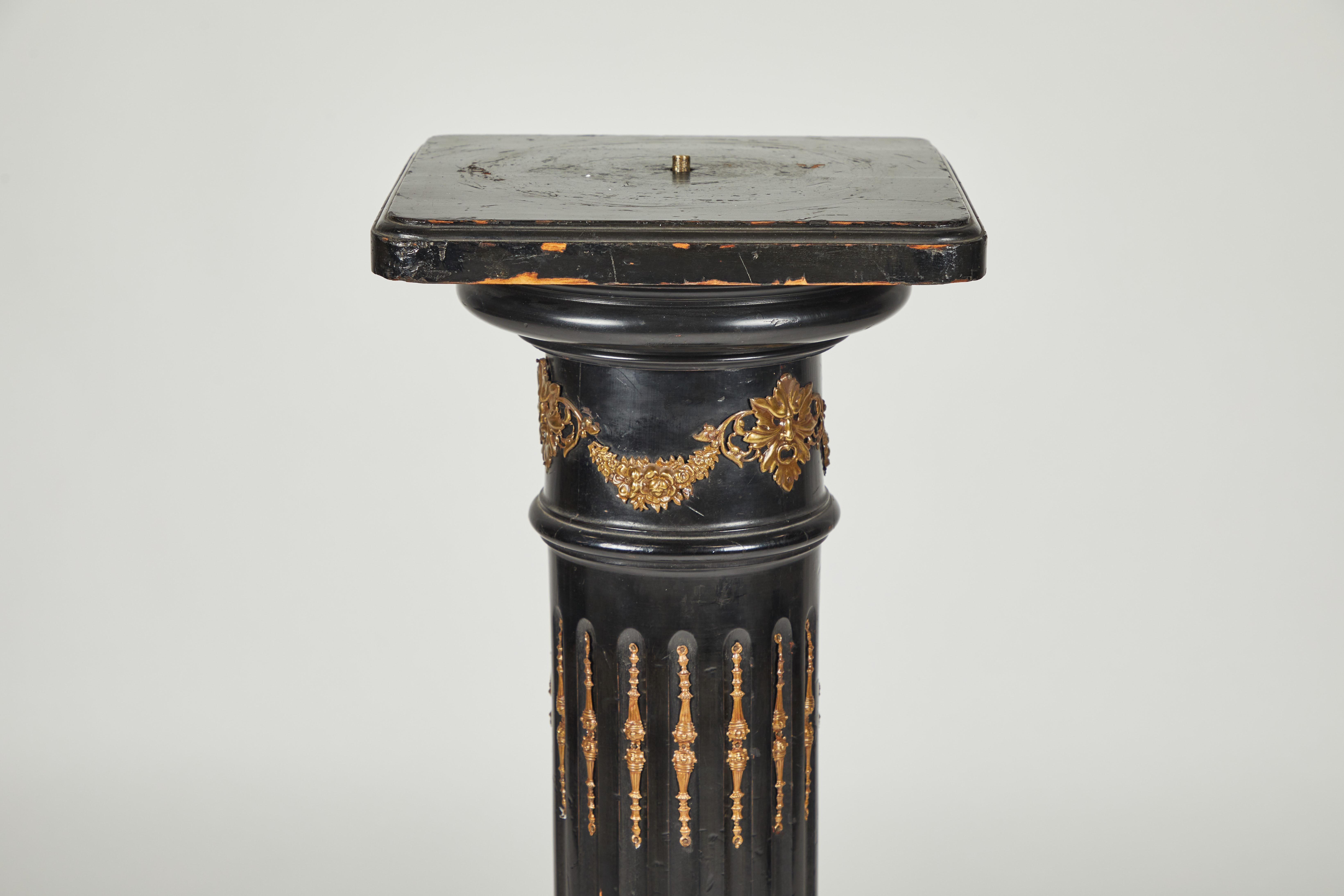 Ebonized Grand Tour Column. Gilded bronze mounts in the form of garland swags and masks surmount a fluted shaft with well-cast decorative mounts, sitting atop a square plinth base.