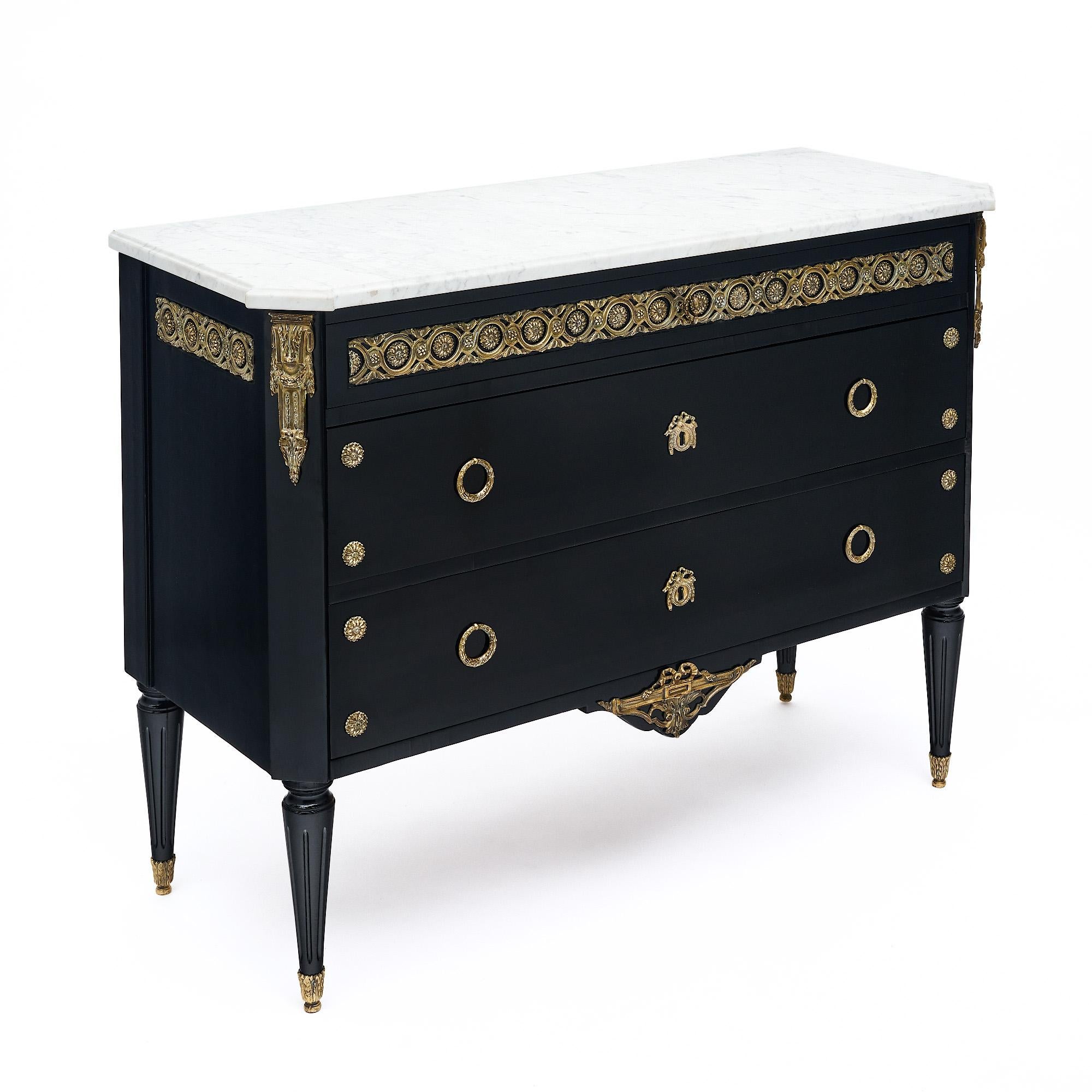 Chest of drawers in the Louis XVI style from France. This piece has been ebonized and finished with a lustrous museum-quality French polish with gilded ormulu throughout. Three dovetailed drawers are all adorned with gilt brass décor and the chest