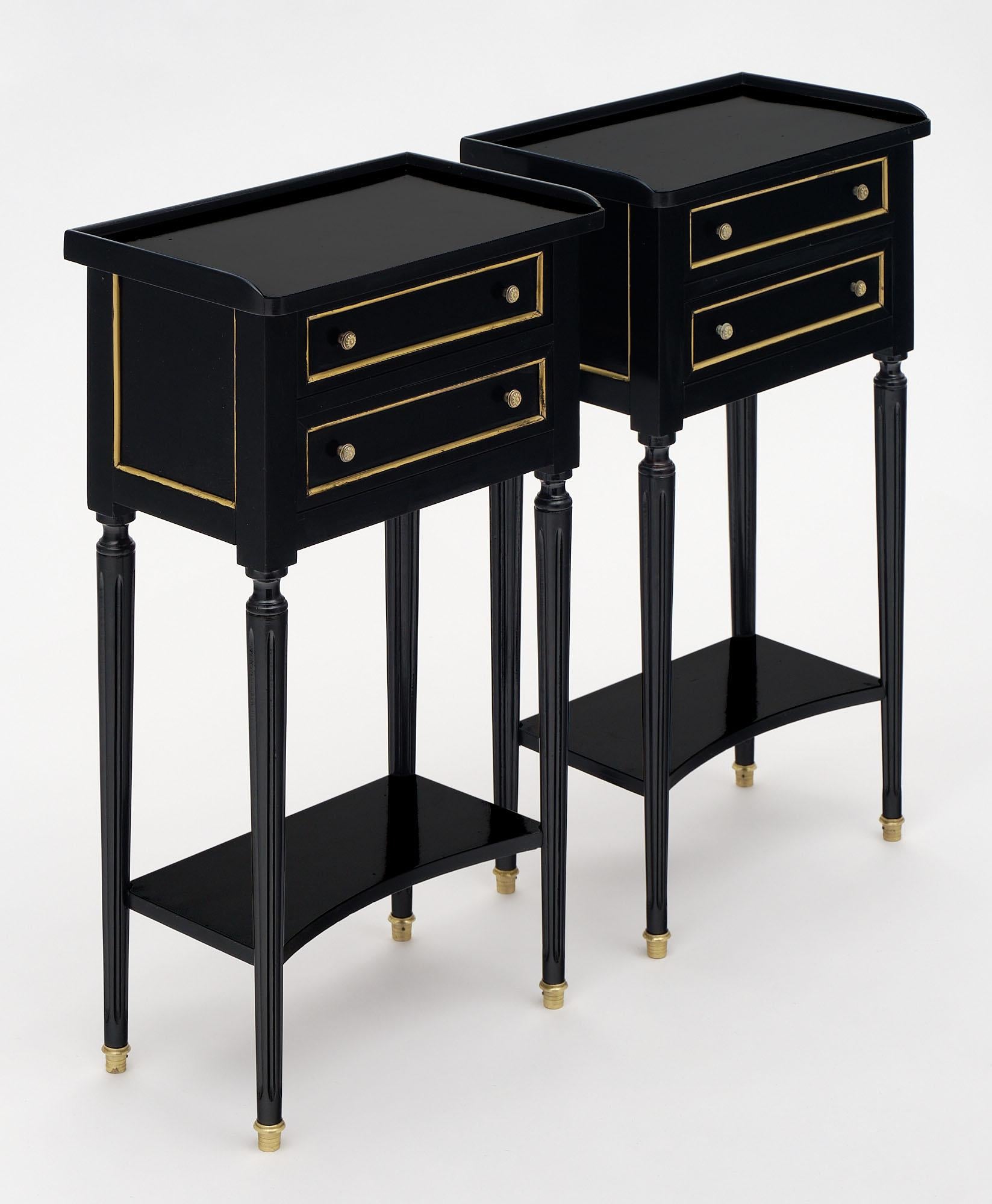 Pair of side tables from France in the Louis XVI style. Each table has two dovetailed drawers with gilt brass trim throughout. They have finely cast bronze knobs. The legs are tapered and fluted with a supportive bottom shelf. They are ebonized and