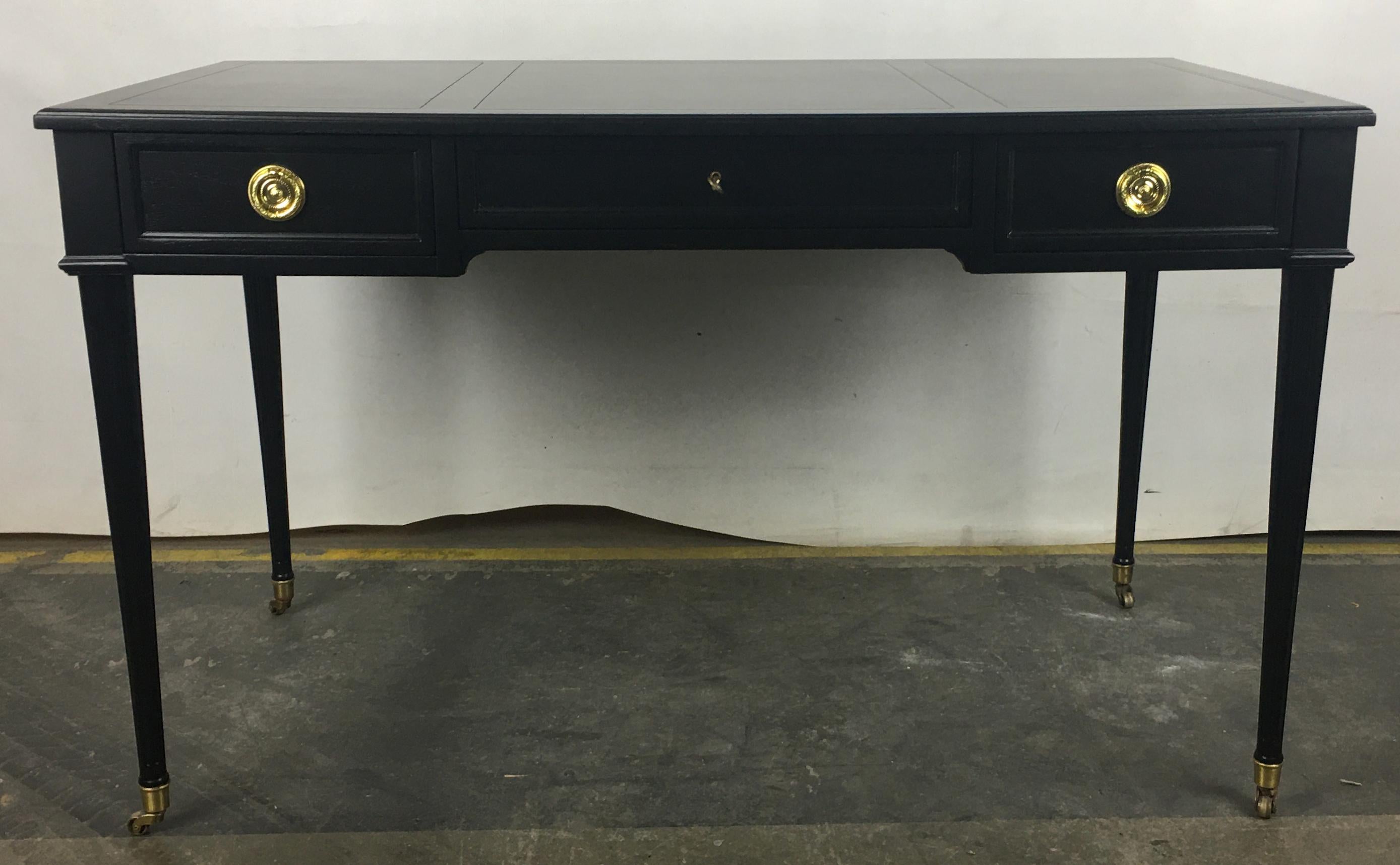 Handsome writing desk in black lacquer by Baker/Milling Road. Features brass hardware and cup casters and the center drawer is both locked and pulls open with the key. The writing surface is wood and divided into three panels. Finished on all sides.
