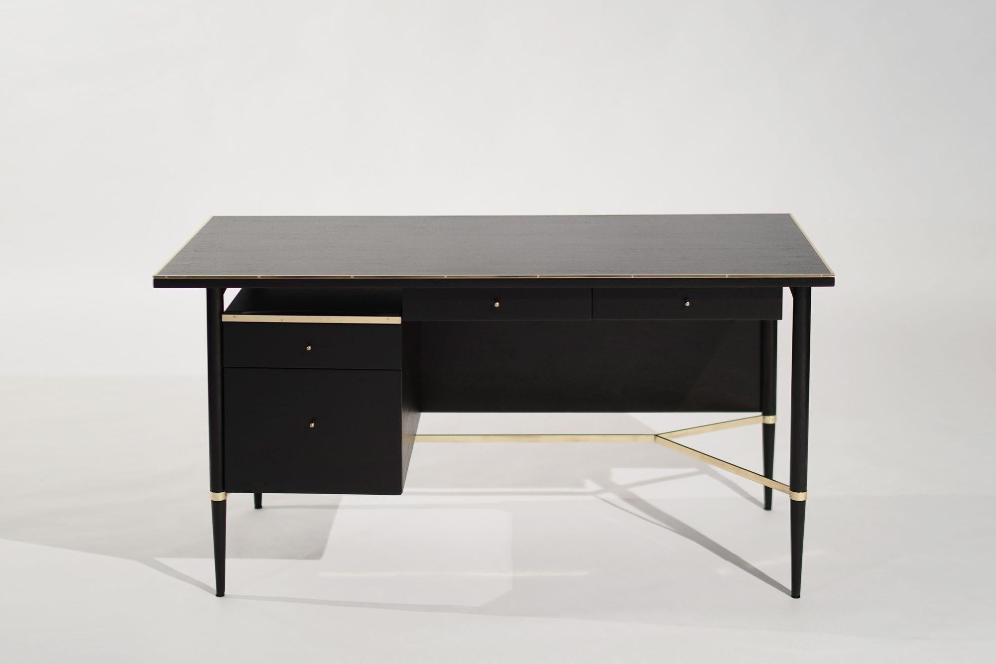 Ebonized Mahogany Desk from Paul McCobb's Connoisseur Collection, meticulously restored by Stamford Modern. Crafted in the 1950s, this mid-century icon boasts minimalistic lines and a sleek silhouette. Brass accents add luxury, emphasizing clean