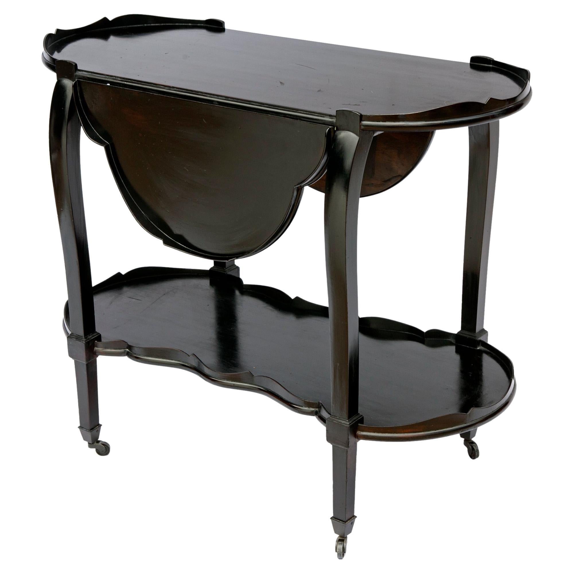 Sleek mahogany bar cart in ebony with lower level, drop leaf top opens to four leaf clover. Scalloped edge on both levels.
Graceful, curved legs on antique brass casters.