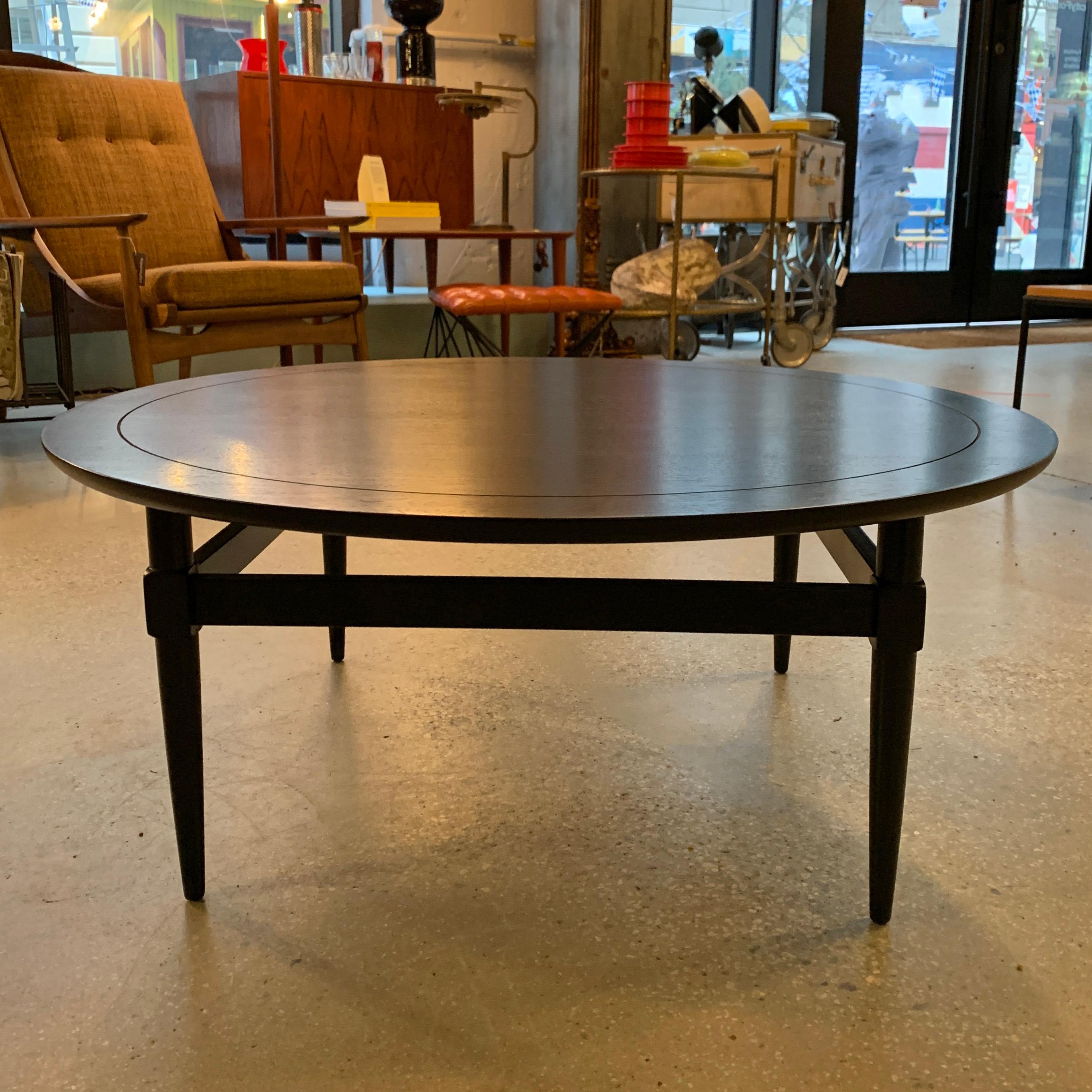 Elegant, midcentury, round, ebonized mahogany, coffee table features a scored top with linked leg detail.