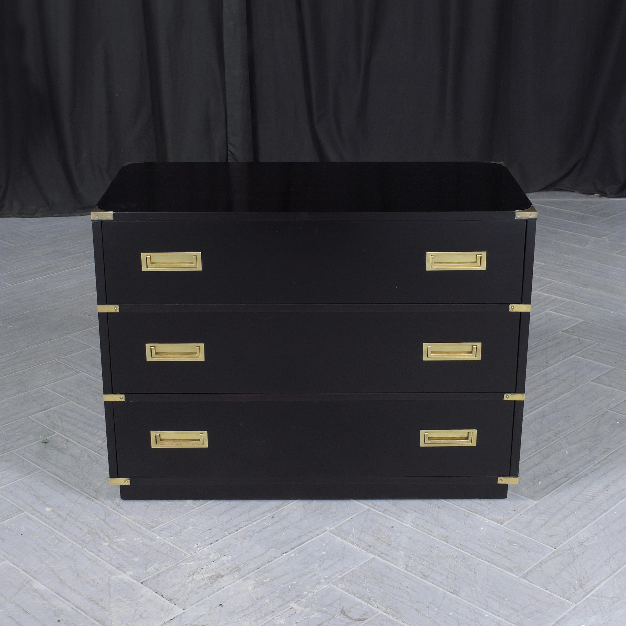 Showcasing our expertly restored Mid-Century Campaign Chest of Drawers, intricately handcrafted from the finest mahogany wood. This chest boasts a rich ebonized black lacquer finish, providing a striking contrast to its original gleaming brass