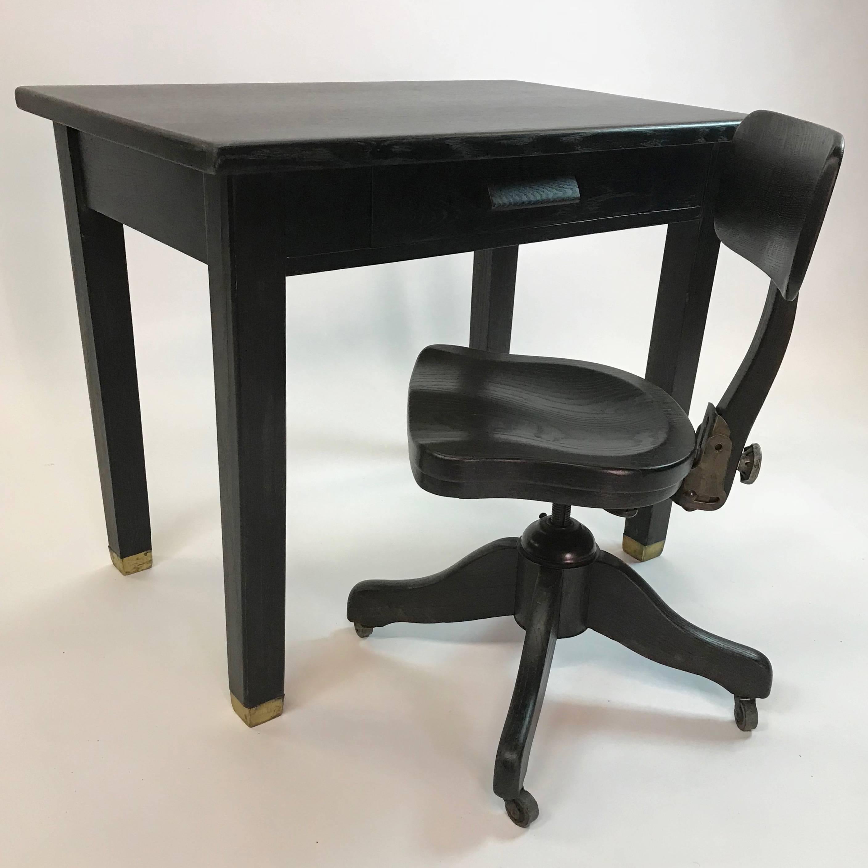 Industrial, ebonized oak, library desk features brass capped legs and is accompanied by a matching, height adjustable, tilt-back, desk chair. The chair's foot print is 24 inches square, seat width is 16 inches, overall depth is 18 inches and height