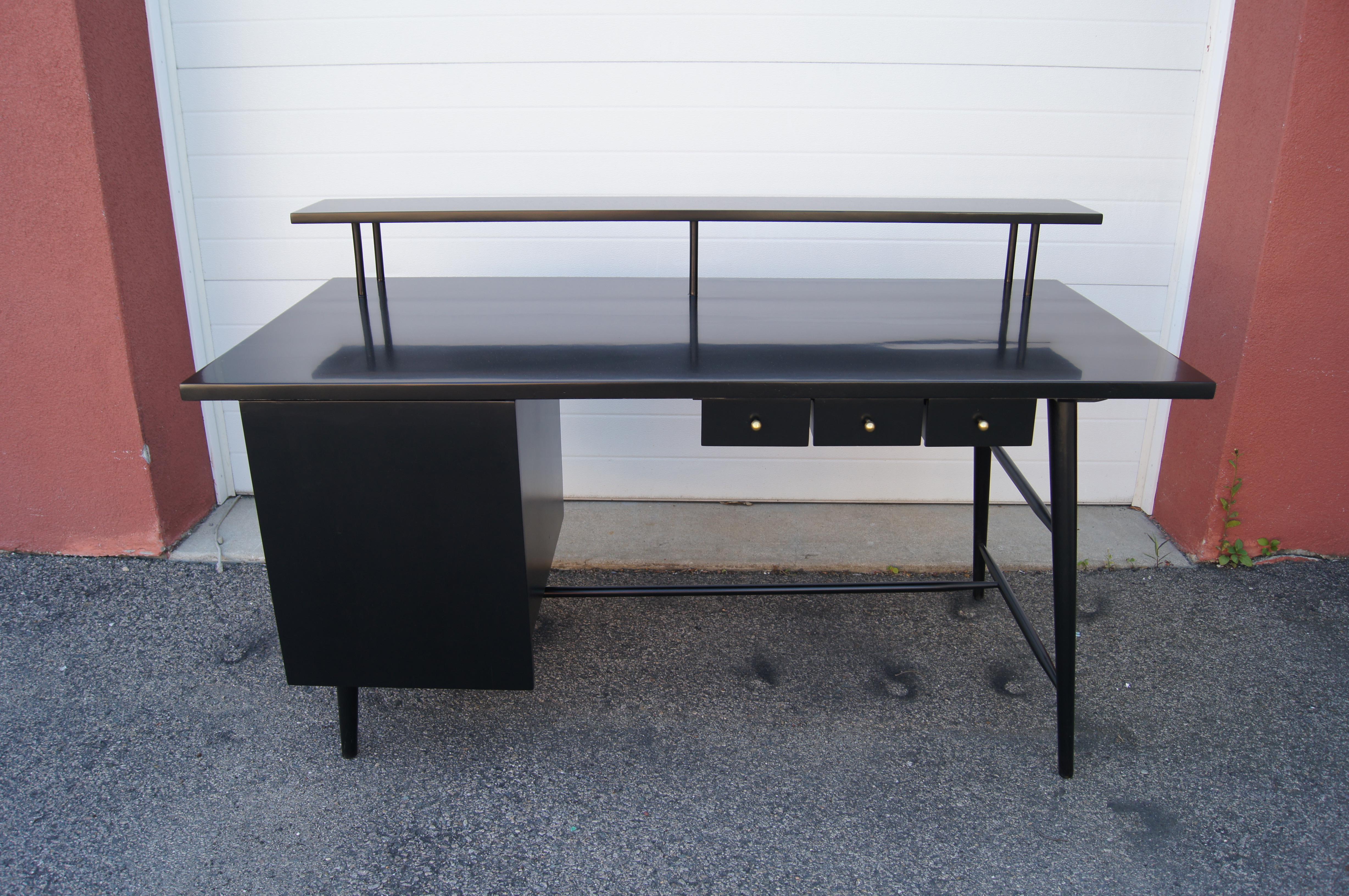 This hard-to-find desk is a Paul McCobb design for his Predictor series, manufactured by O'Hearn Furniture only from 1951 to 1955. The ebonized maple case sits on slender canted legs. To the left a door conceals three drawers, the lower of which is
