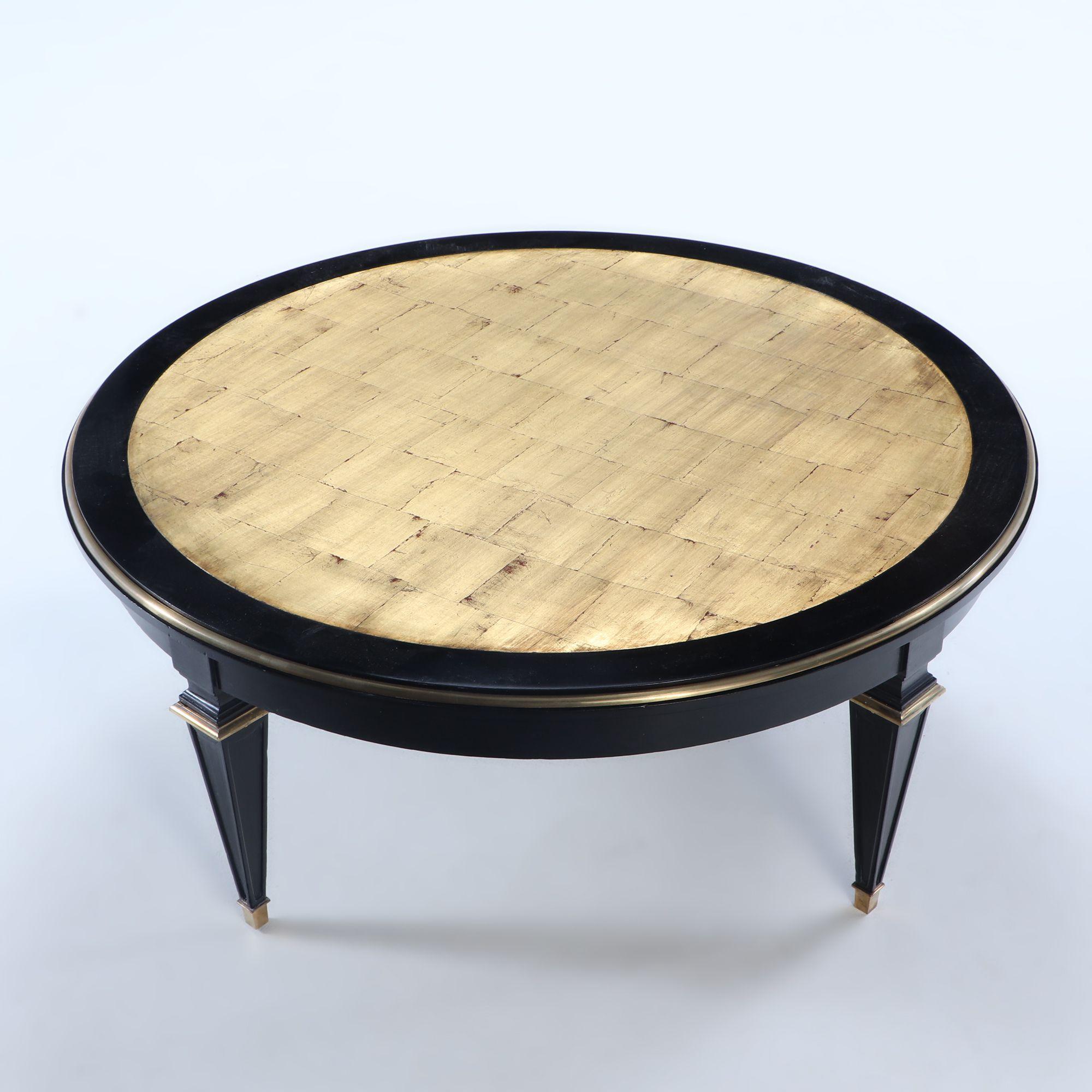 An ebonized round coffee table in the manner of Jansen having a gold gilt wood top trimmed in bronze and bronze mounted legs, circa 1940.