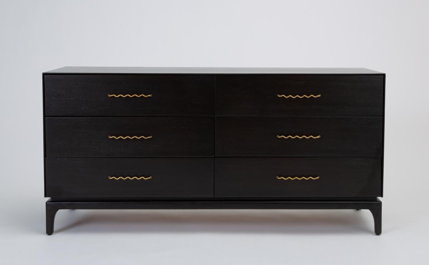 A modest dresser in ebonized mahogany designed by John Keal and produced by Brown Saltman has six drawers in a slender case, perched on a frame with four petite, sculpted legs. The piece's most distinctive attributes are its whimsically curled