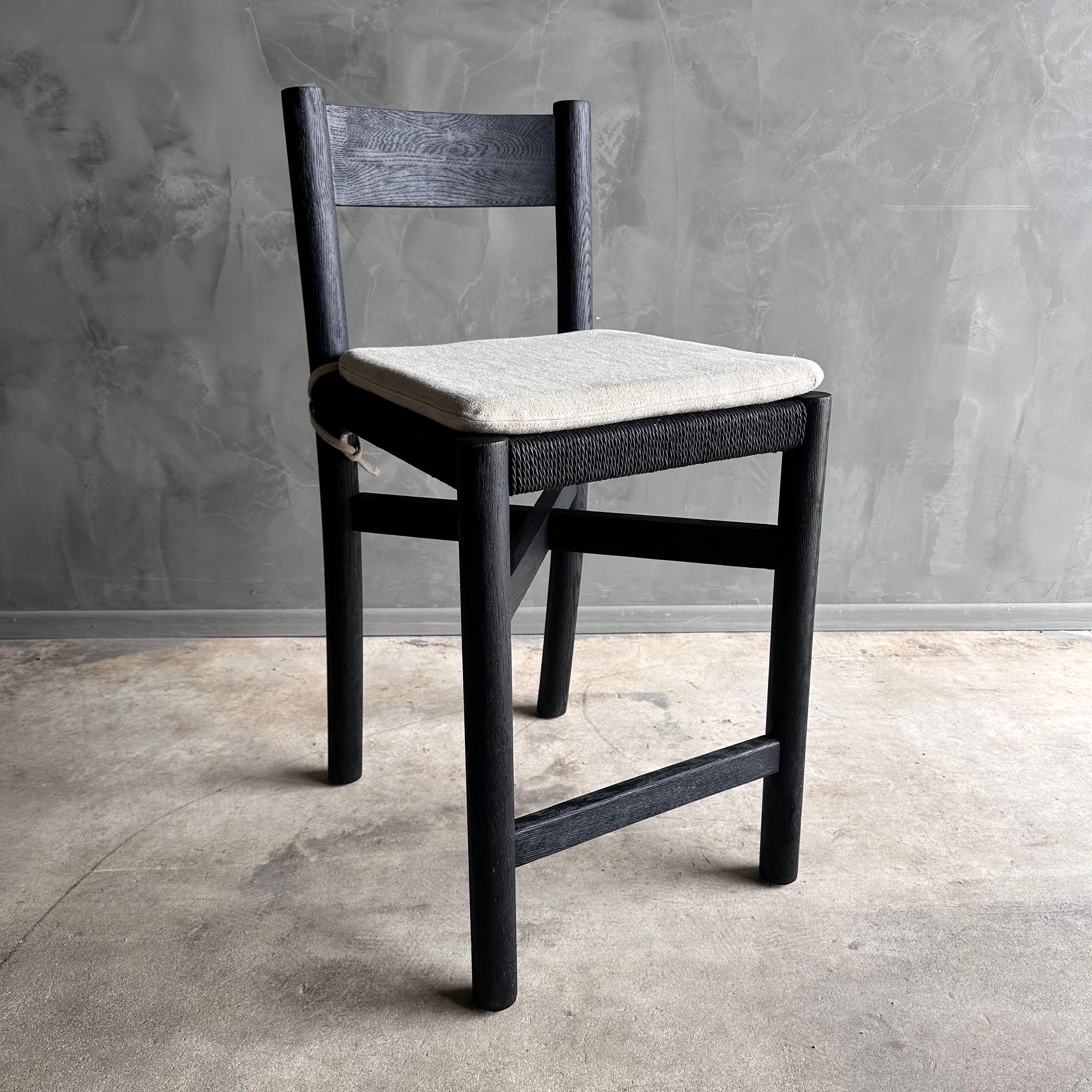 Ellie Counter Stool in ebonized white oak and flax linen cushion
Elevate your kitchen or bar space with the Ellie Counter Stool. Made from solid white oak with an ebonized finish, this stool boasts a woven seat and a sturdy wood frame with a