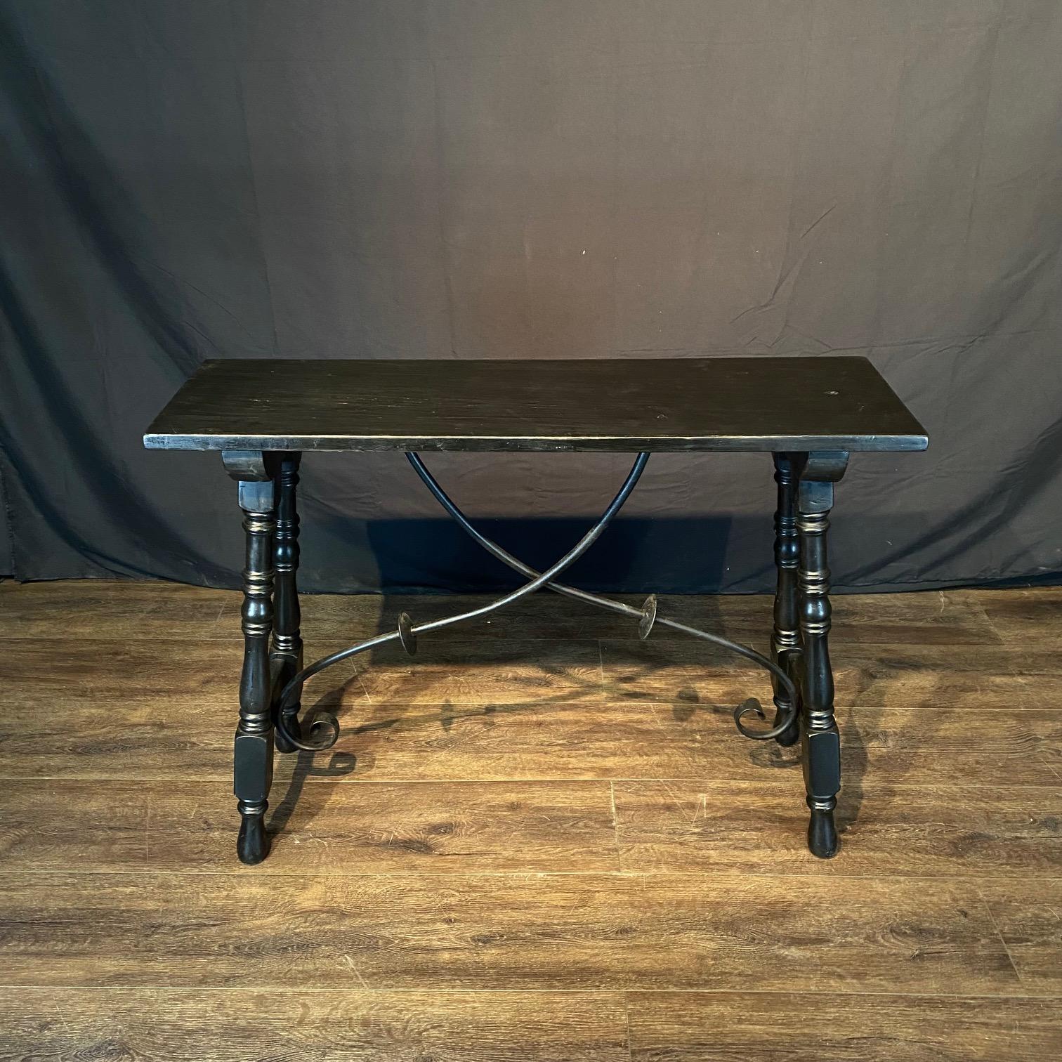 Bought in France, this lovely Spanish black console table boasts hand made wrought-iron stretchers. This classic accent table features a sturdy long rectangular top sitting above an exquisite base made of splayed carved and turned legs connected to